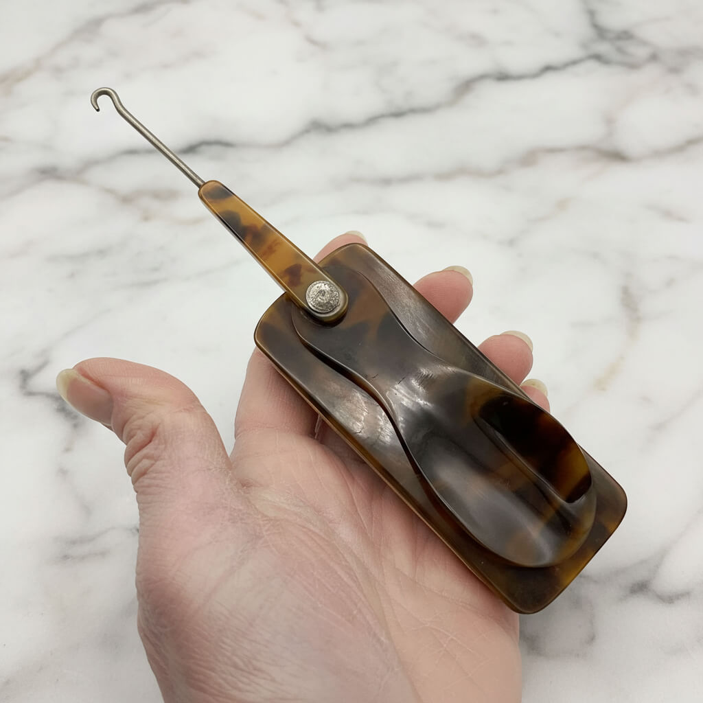 Button hook horn and buffer held in hand with a marble background