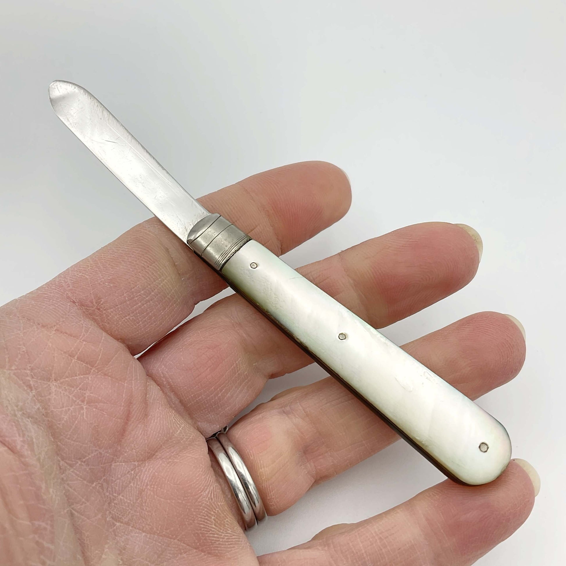This is s folding fruit knife with a silver blade and a mother of pearl handle held in a hand.