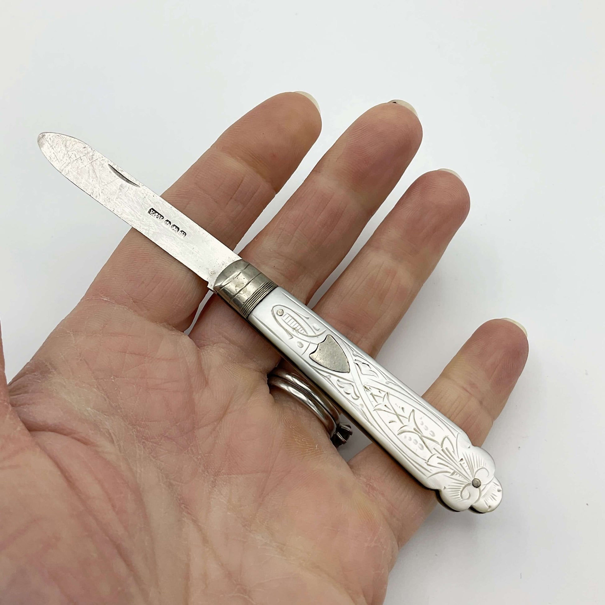 Vintage silver fruit knife with a beautifully engraved mother of pearl handle held in a hand