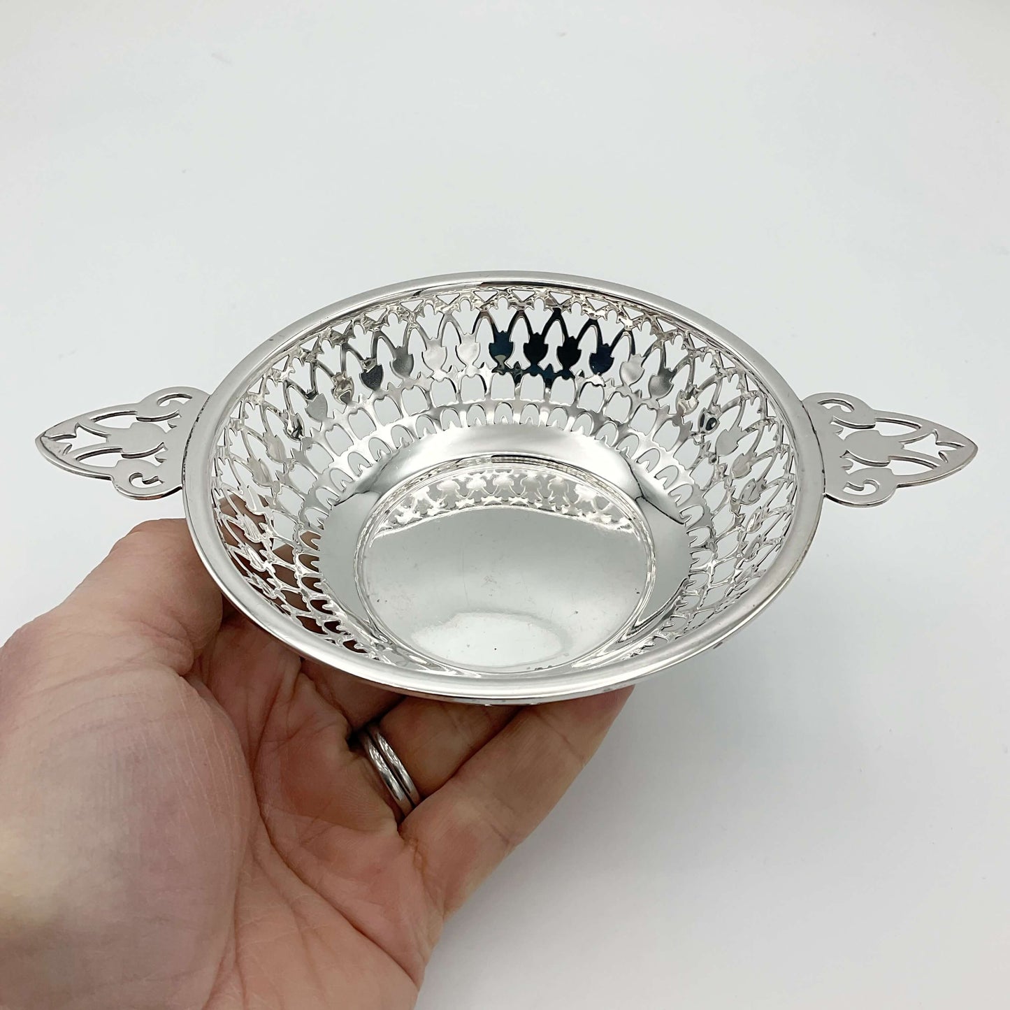 Shiny silver pierced bowl with handles sitting in a hand