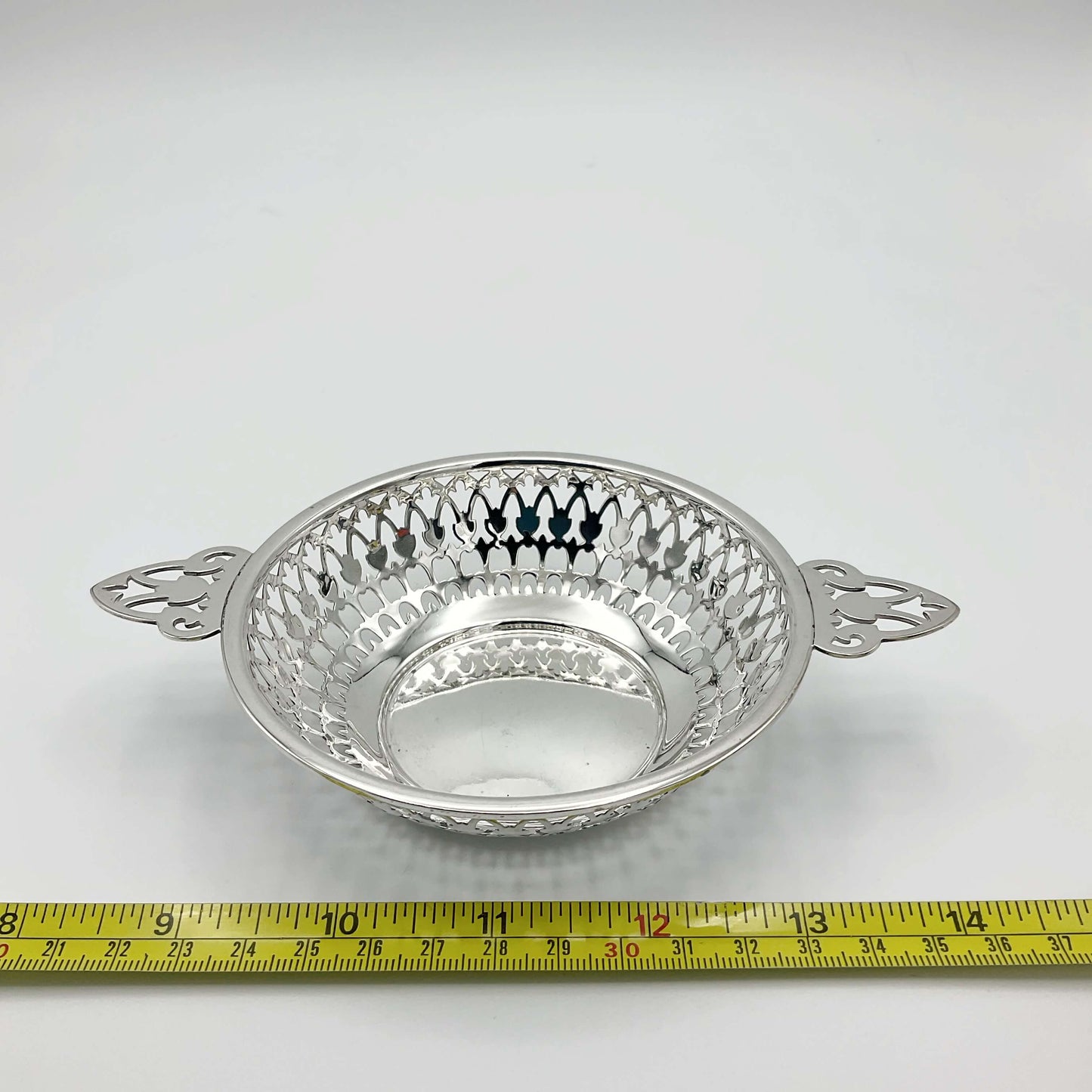 Shiny silver pierced bowl with handles next to tape measure showing width approximately 15cm