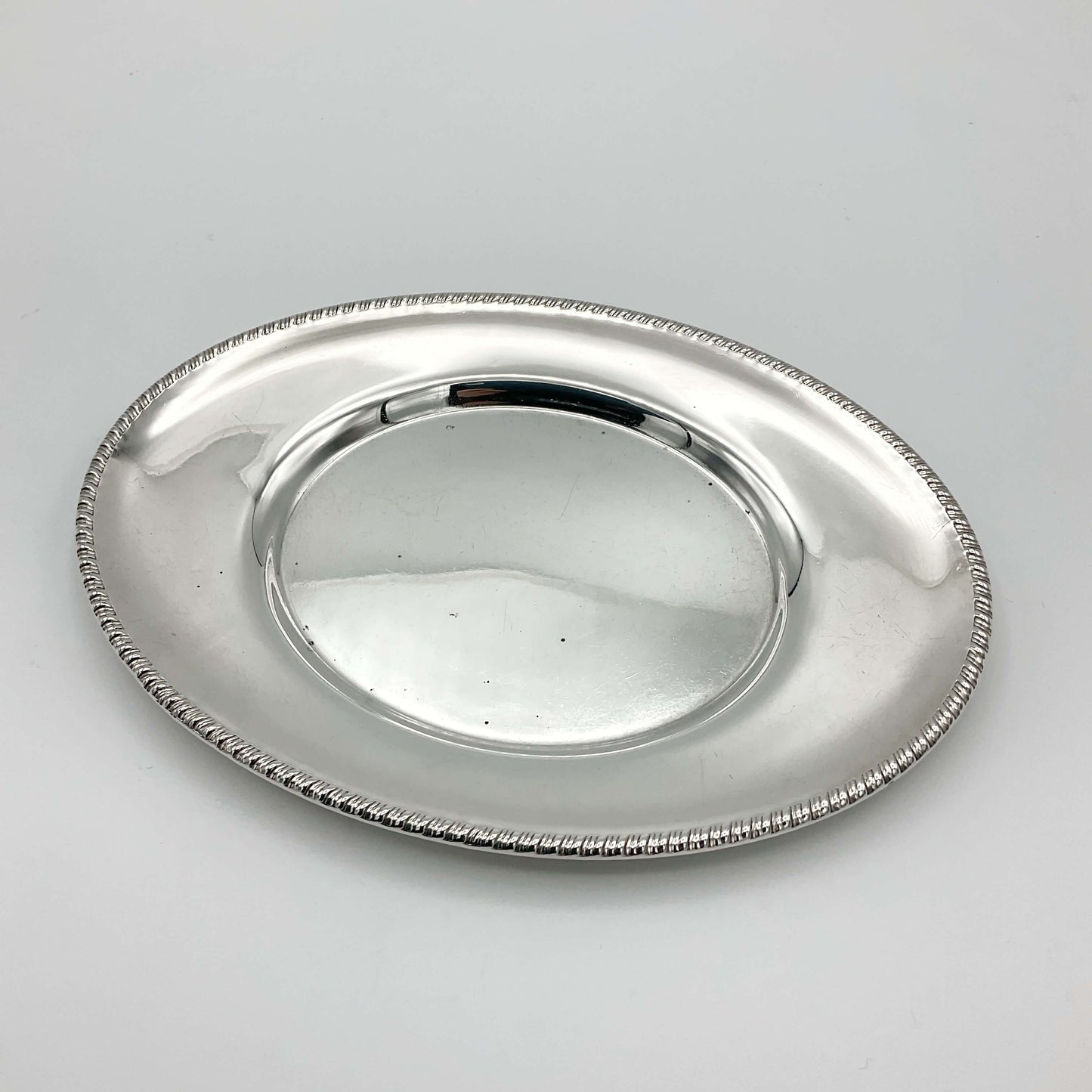 A beautiful shiny silver plated serving tray or platter showing a pretty rope design rim on a white background