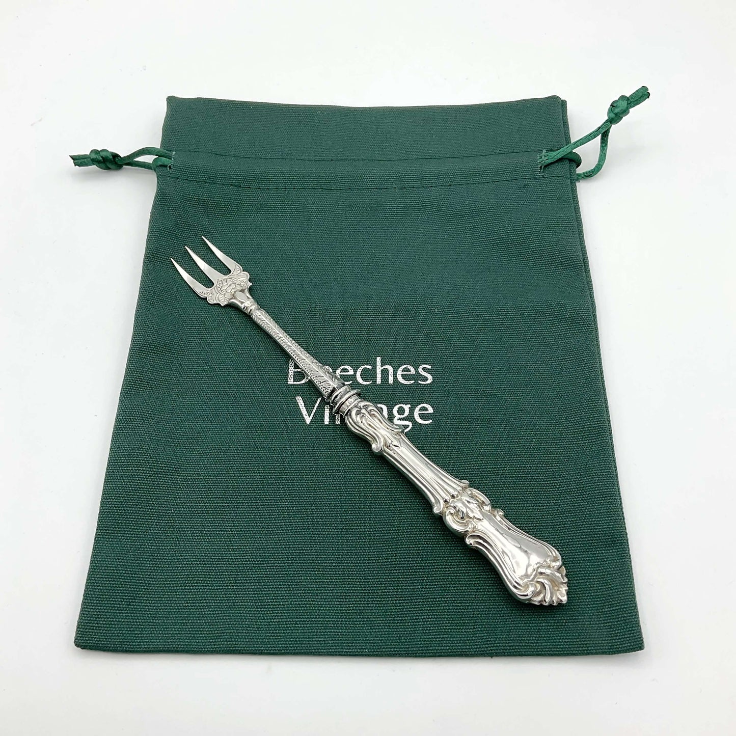 Antique silver plated pickle fork on green cotton gift bag