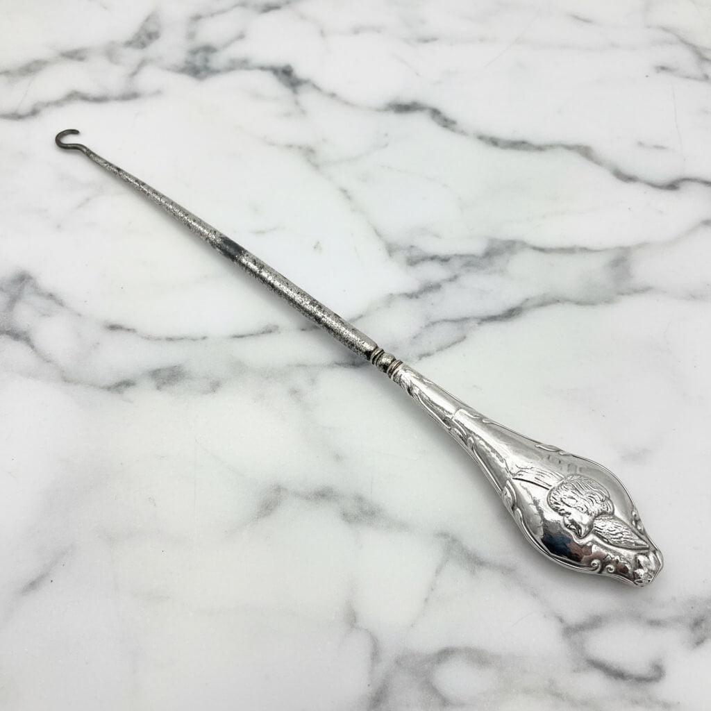 close up of a winged cherub on the silver handle of the button hook