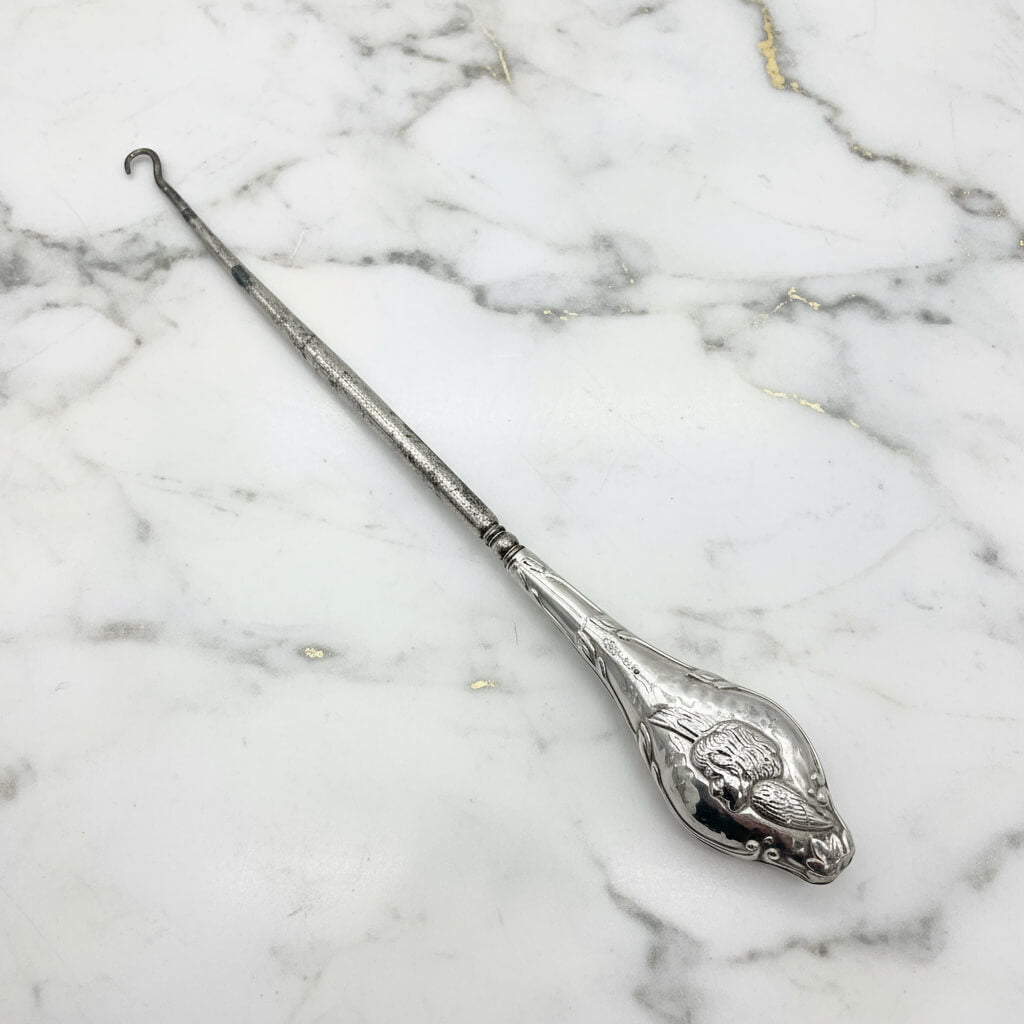 close up of a winged cherub on the silver handle of the button hook