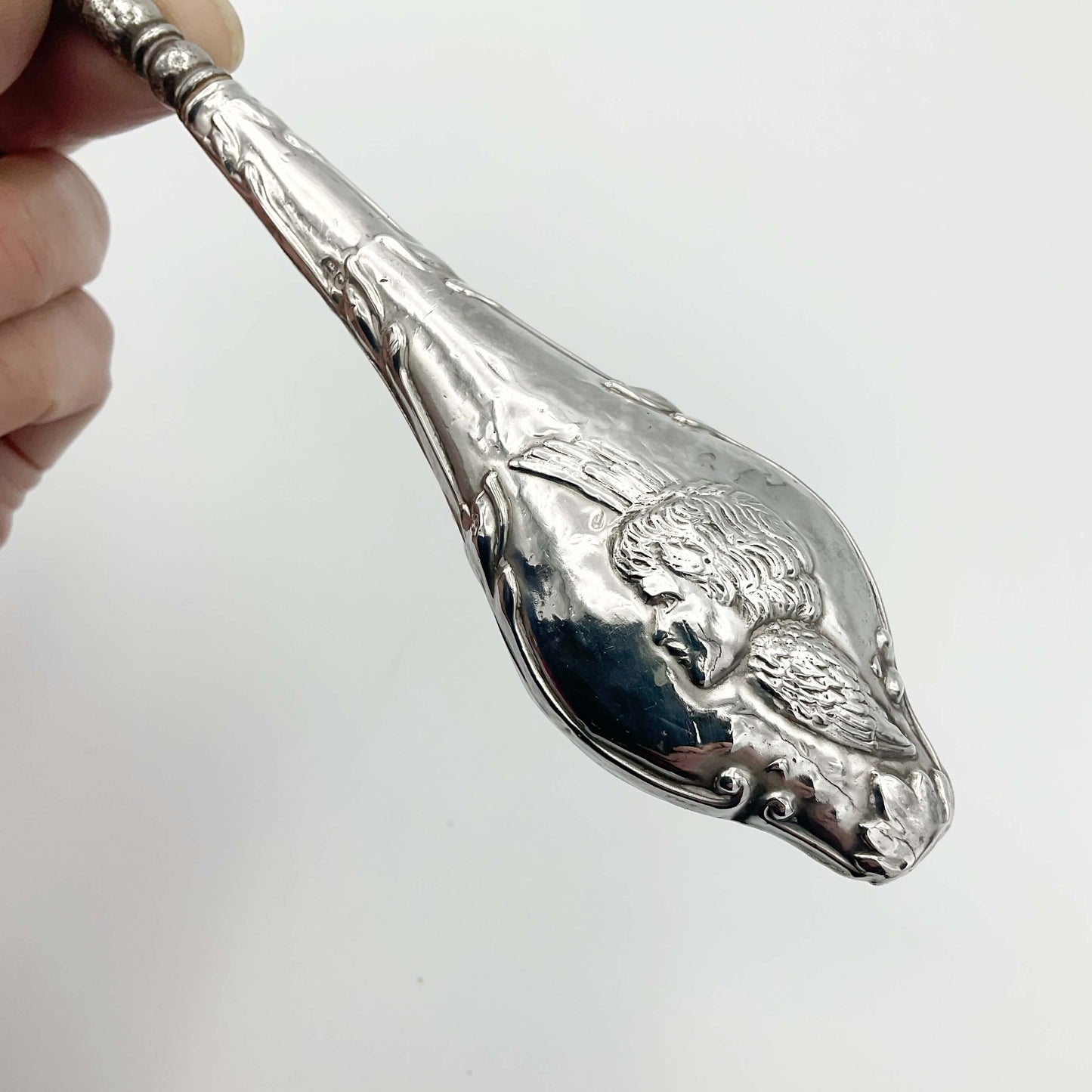 close up of a winged cherub on the silver handle of the button hook
