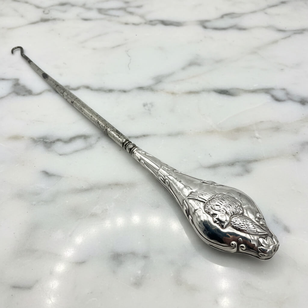 Beautiful large antique silver button hook featuring a cherub on the handle on a marble worktop