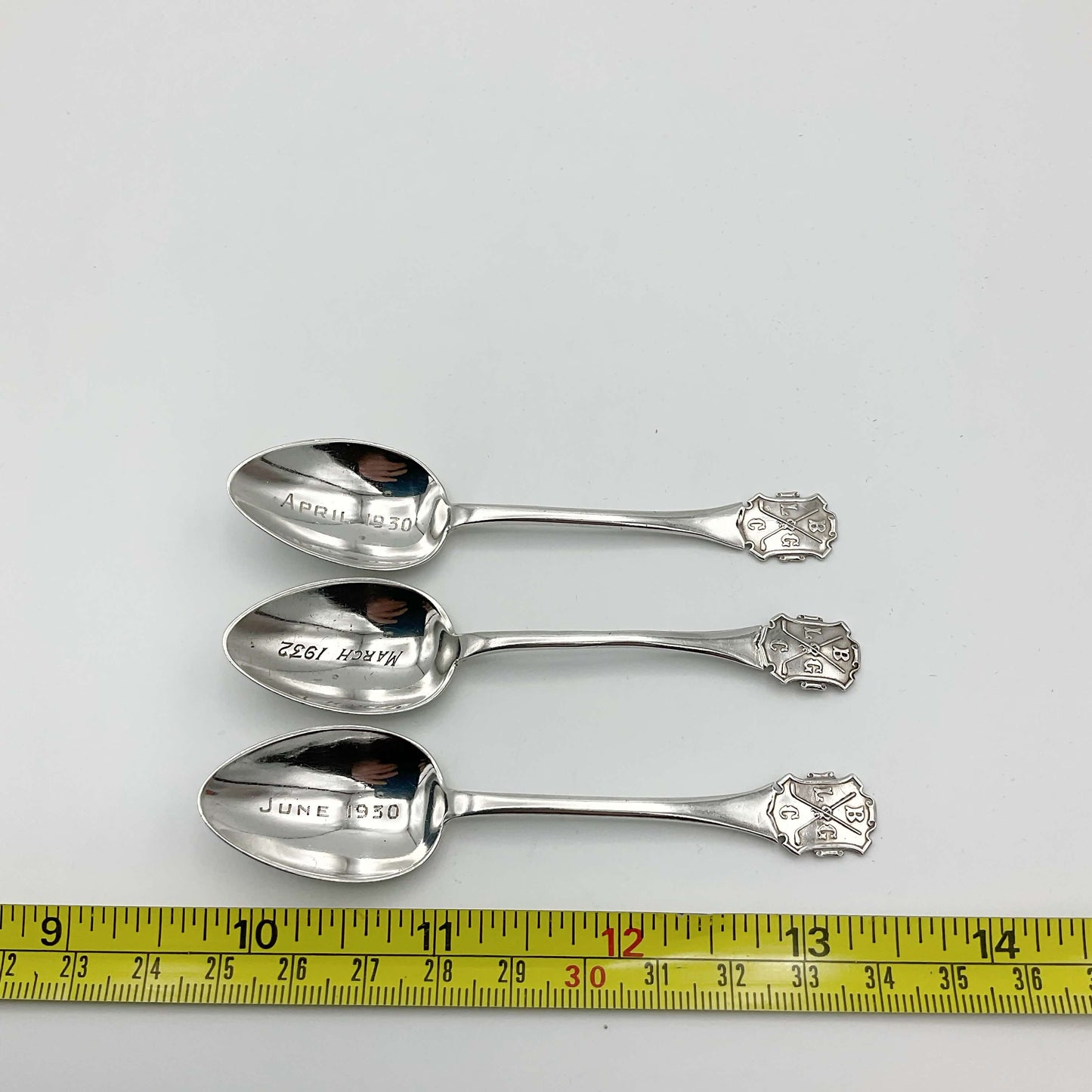 Three vintage silver coffee spoons next to a tape measure showing the length as 9.6cm