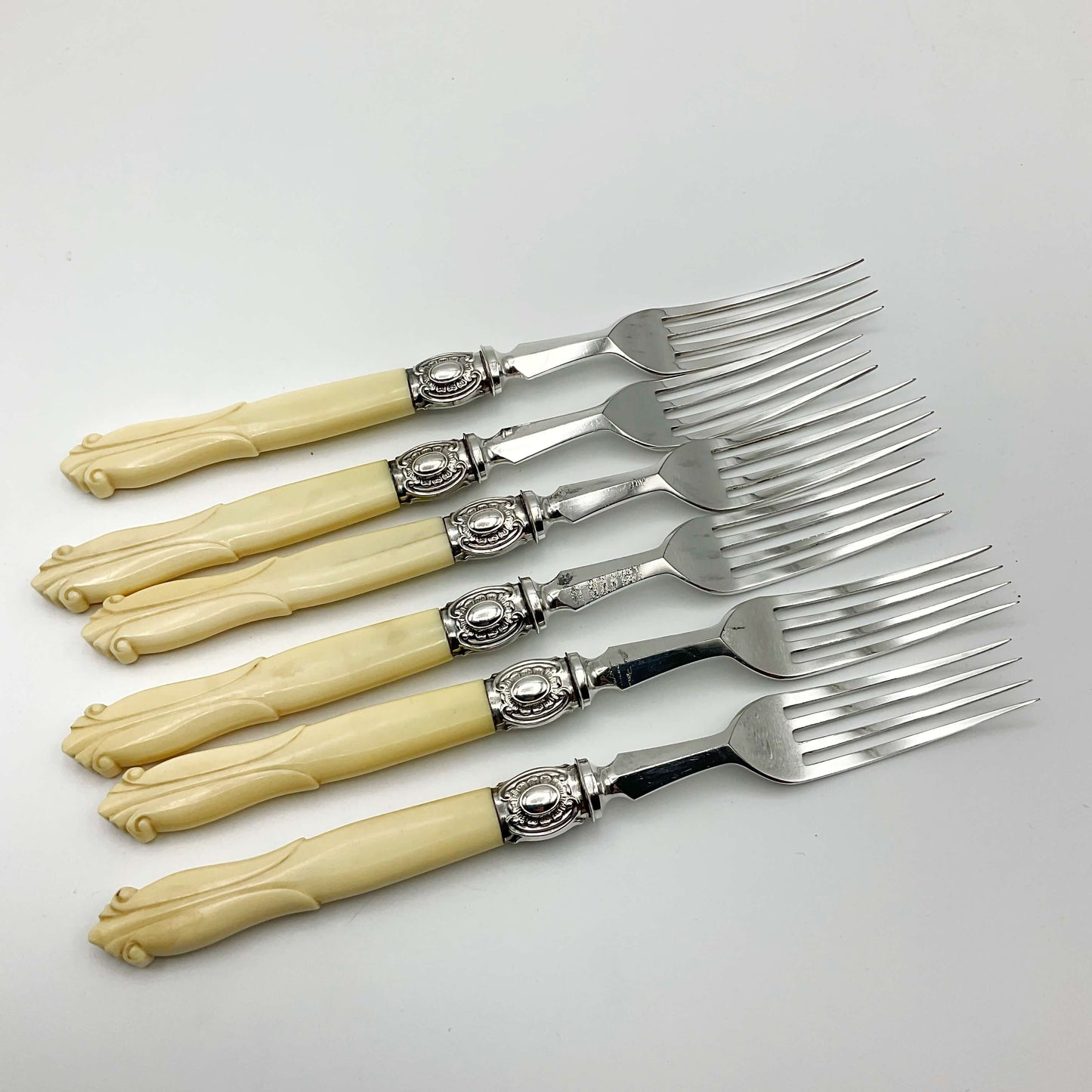 row of six dessert forks with bone handles on a white background