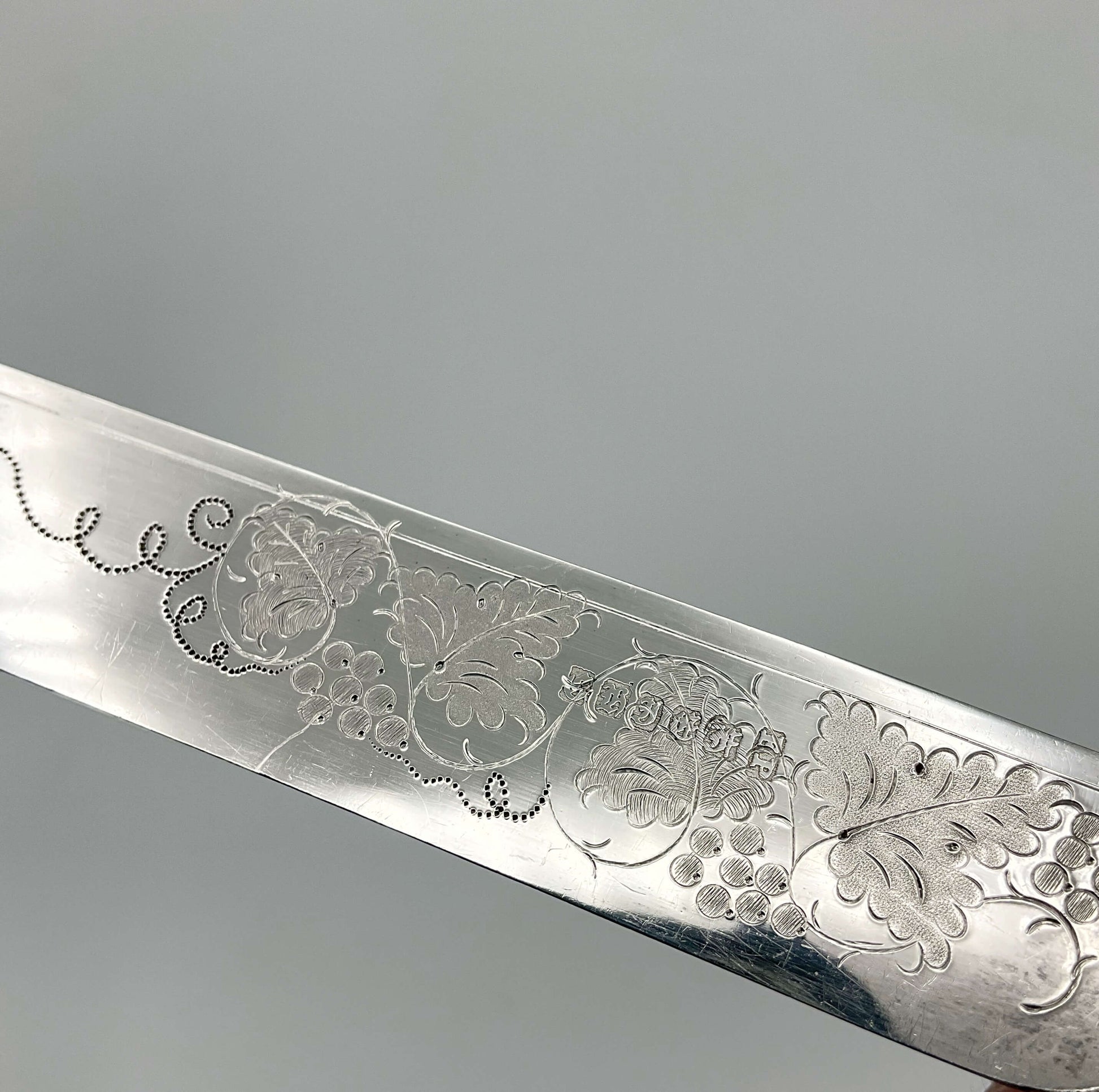 a grape and vine engraved design with the makers mark on a dessert knife blade