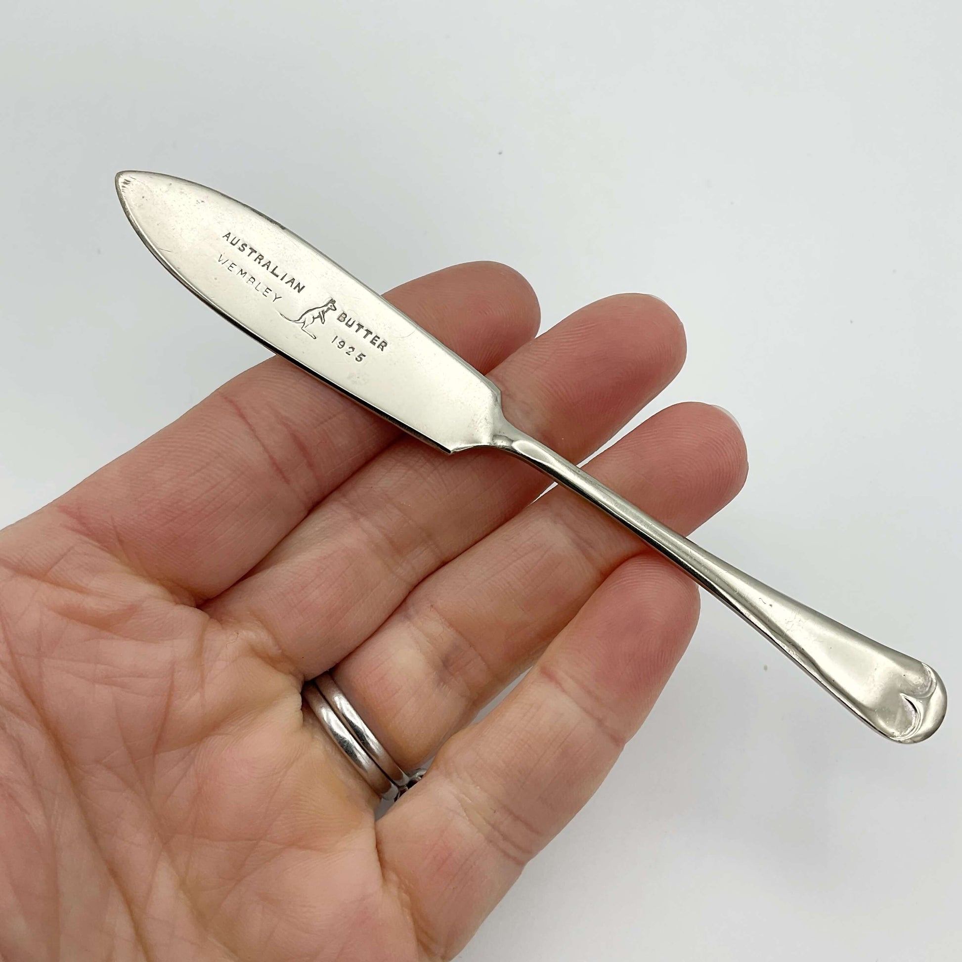 Silver plated butter knife with Australian Butter Wembley 1925 on the blade with a Kangaroo emblem held on a hand