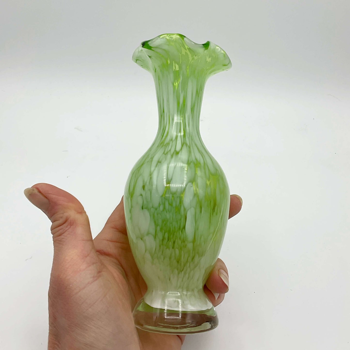 Green and white Murano glass bud vase from the 1960s held in a hand on a white background 