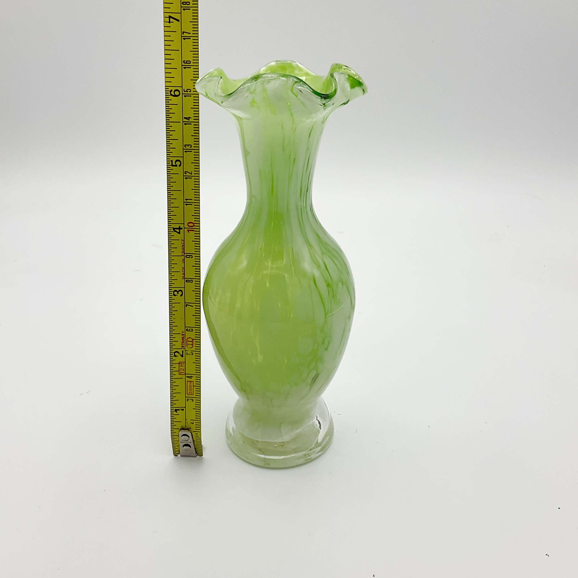 Green and white Murano glass bud vase from the 1960s on a white background Next to a tape measure showing it’s height as 16cm