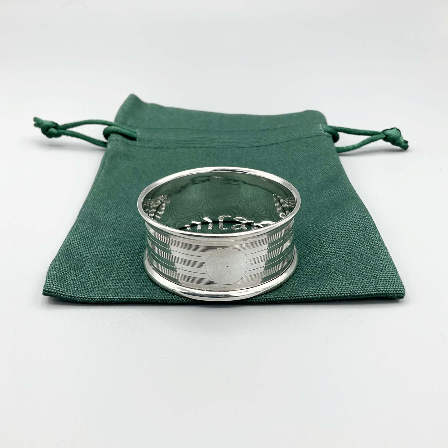 Silver napkin ring with a circular cartouche on a green cotton bag