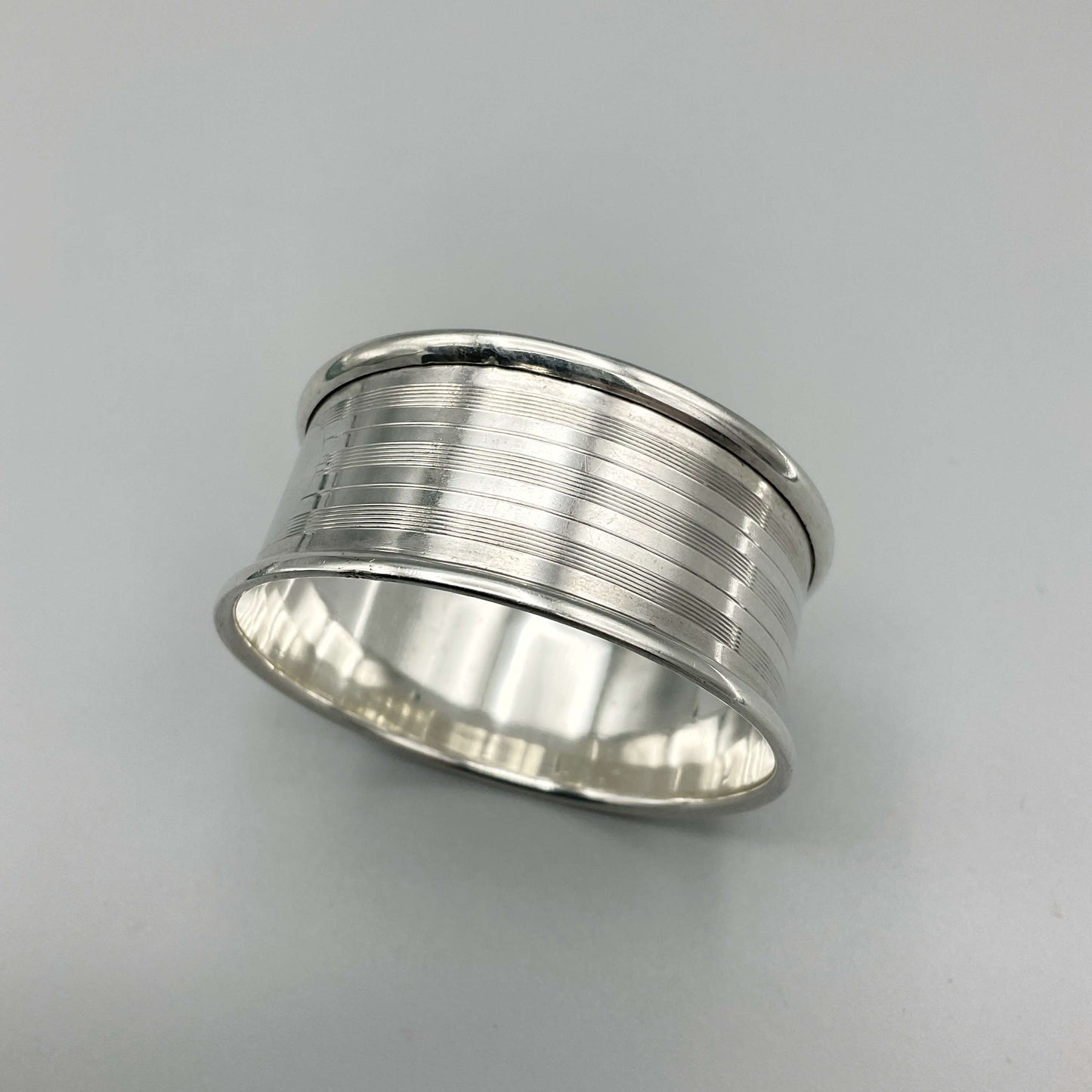 Silver napkin ring with a lined design on a plain background 