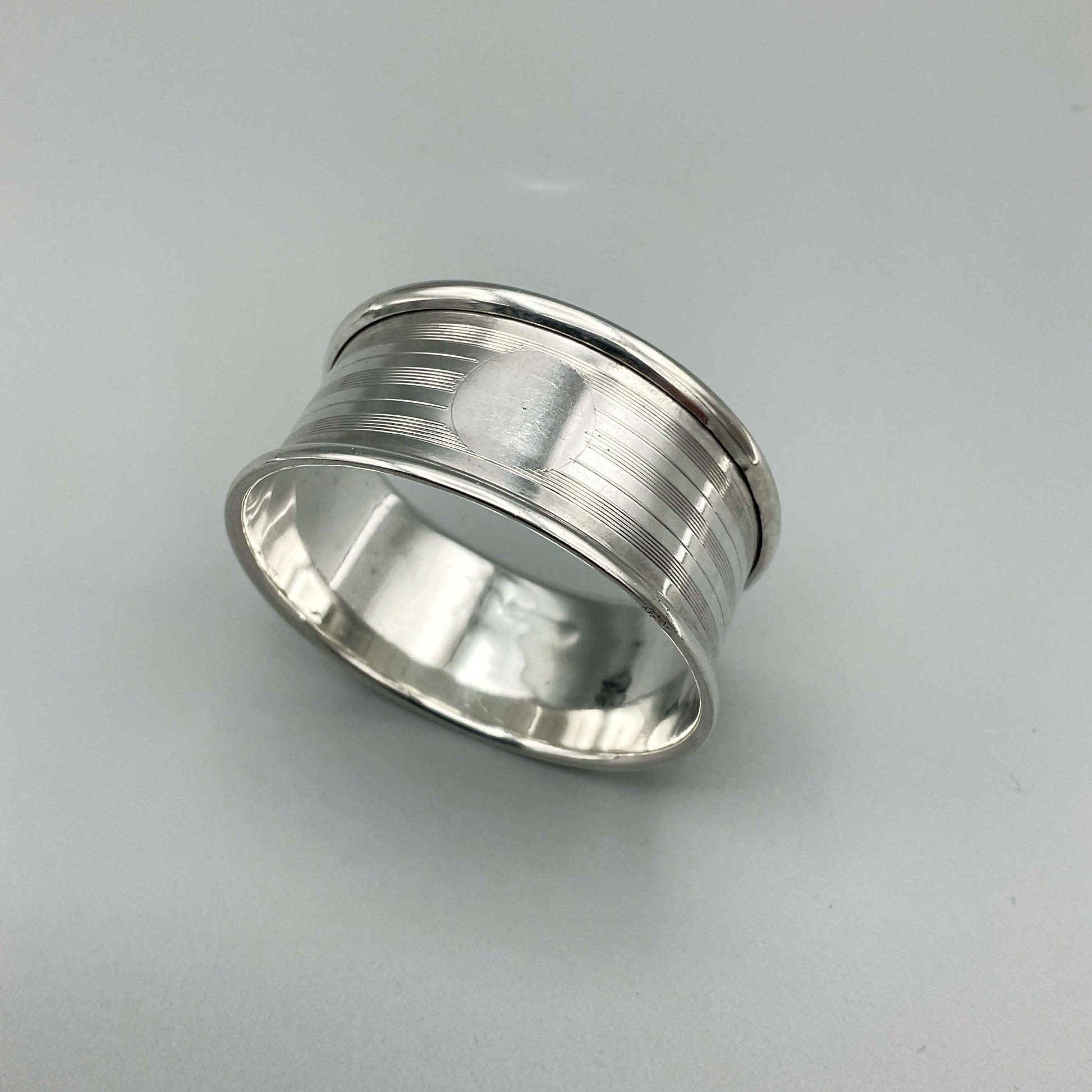 Silver napkin ring with a circular cartouche on a plain  background 