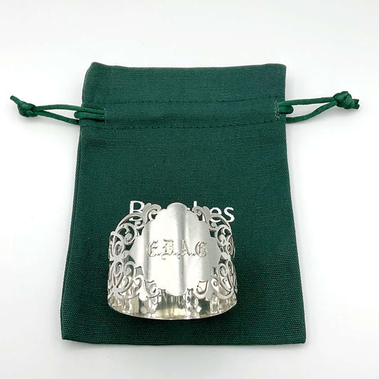 Shiny napkin ring with elaborate sides and EDAG in the centre, sitting on a green cotton bag that has Beeches Vintage on it.