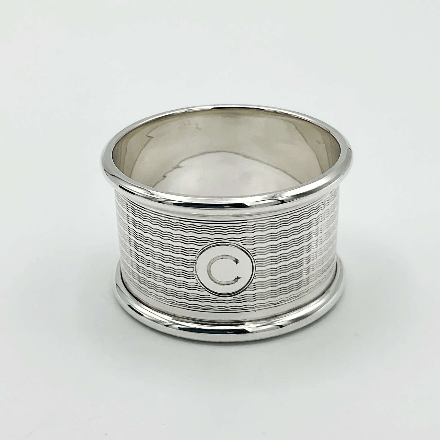Vintage silver napkin ring with C in the centre on a plain background.