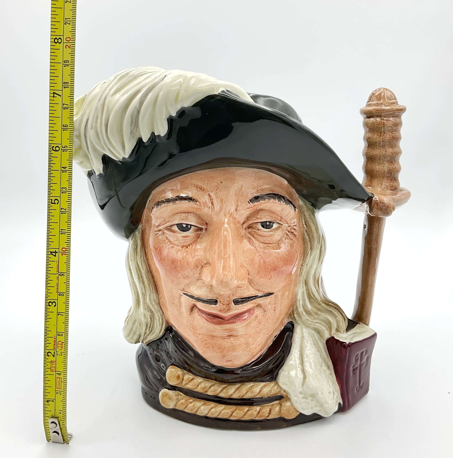 Large Aramis China collectible toby jug on plain background next to a tape measure.