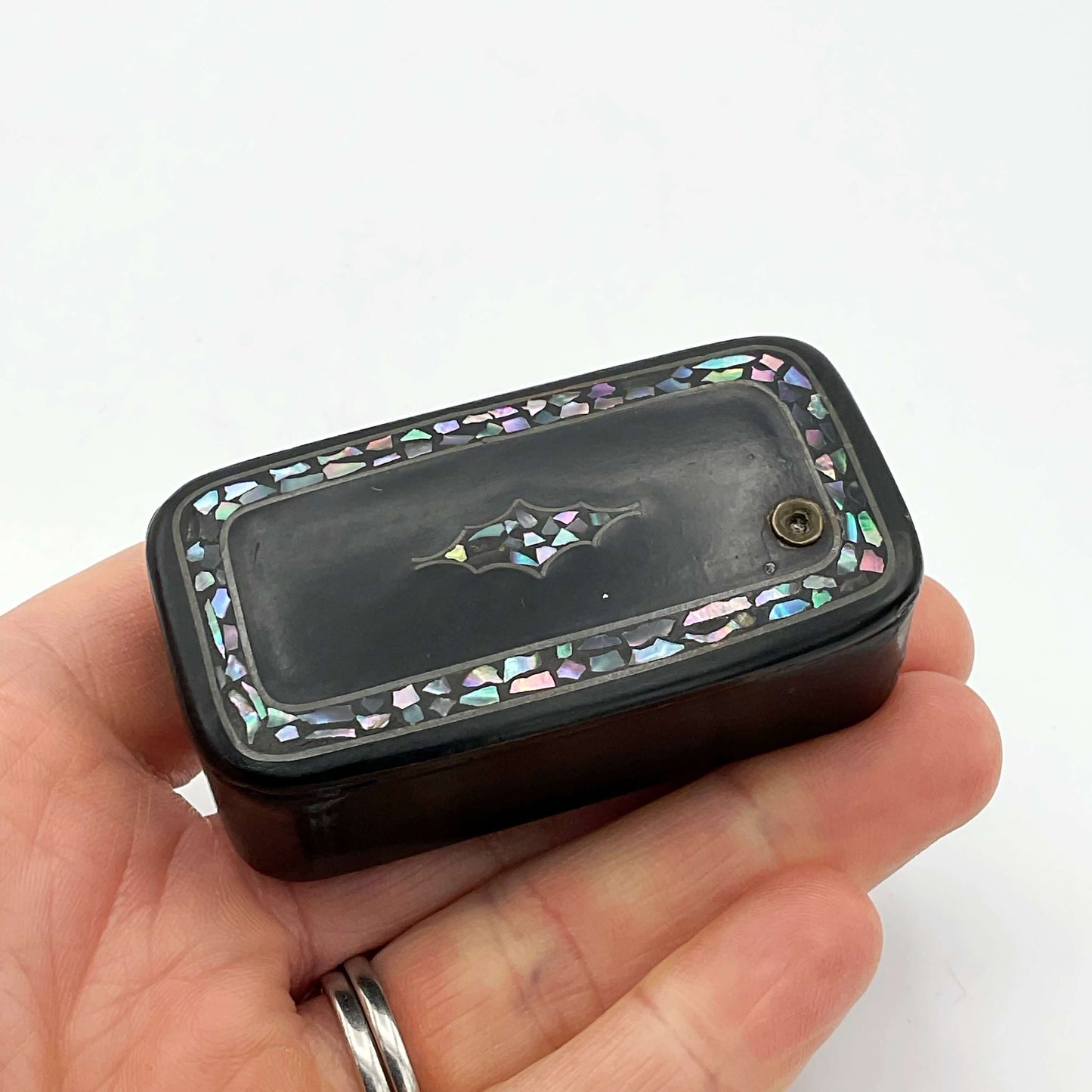 Antique black lacquer snuff box with multicoloured shell inlay held in a hand