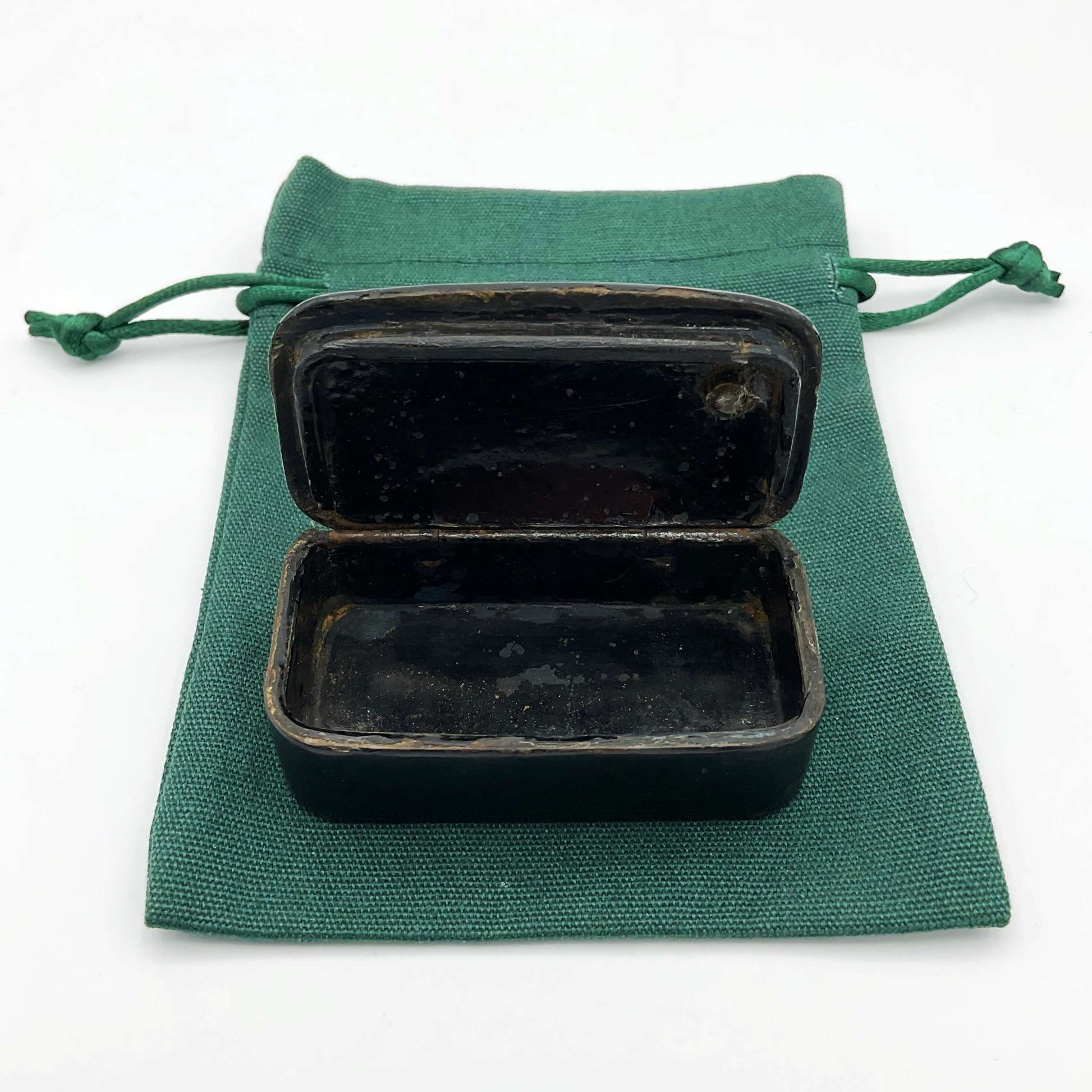 Lid open of Antique black lacquer snuff box showing interior on a green gift bag