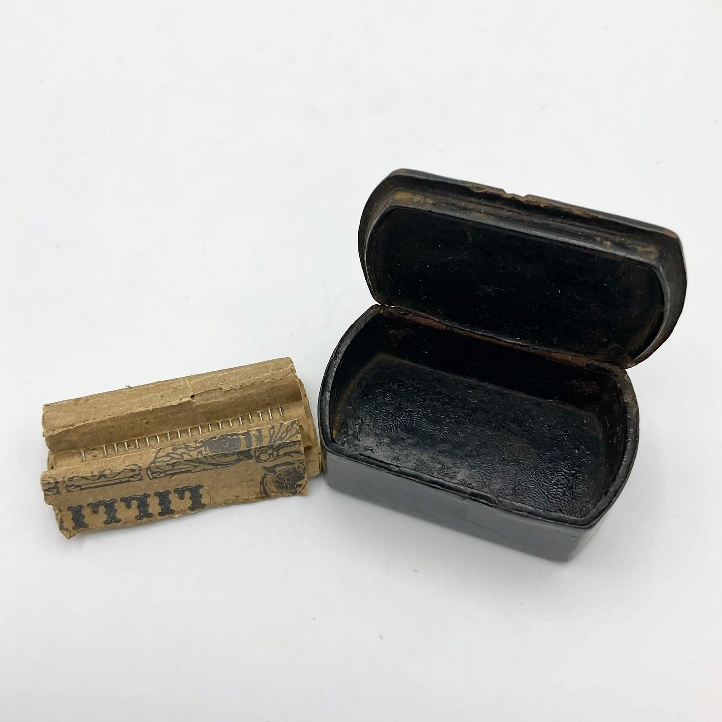 Antique black lacquer snuff box next to Lillikin pins on a paper