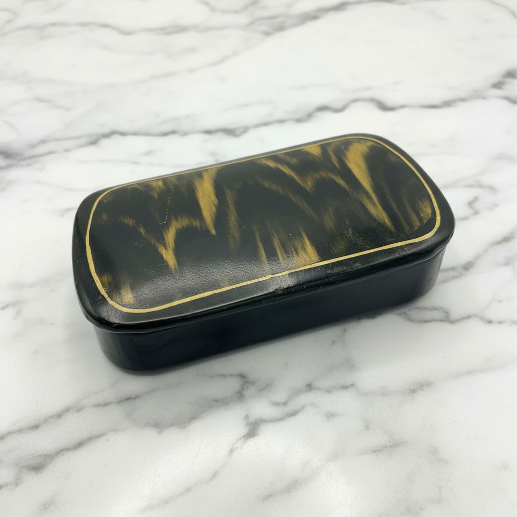 Antique black lacquer and gold snuff box on a marble surface