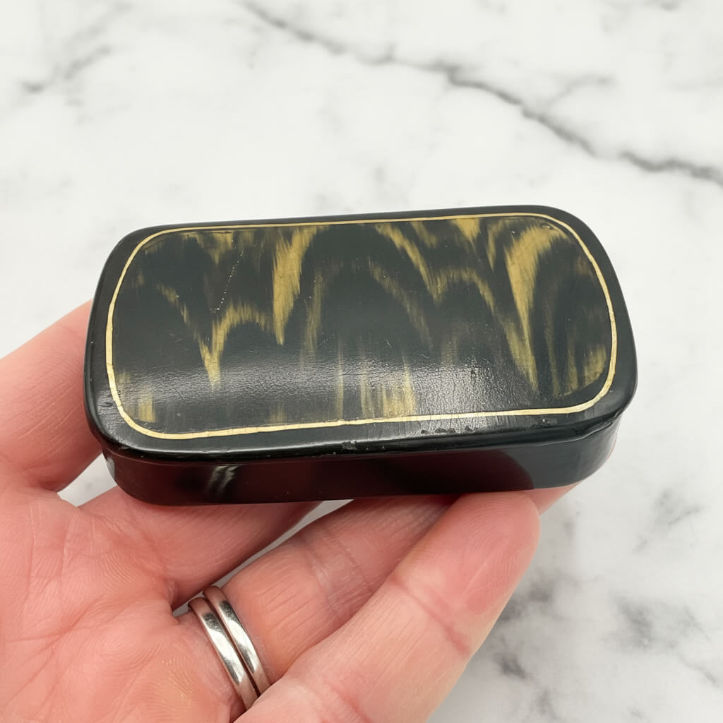 Antique black lacquer and gold snuff box held in a hand