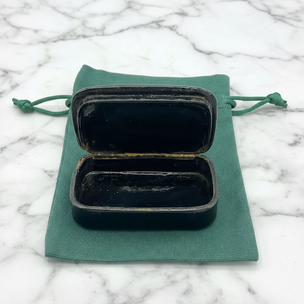 Antique black lacquer and gold snuff box showing the inside on a gift bag on a marble surface
