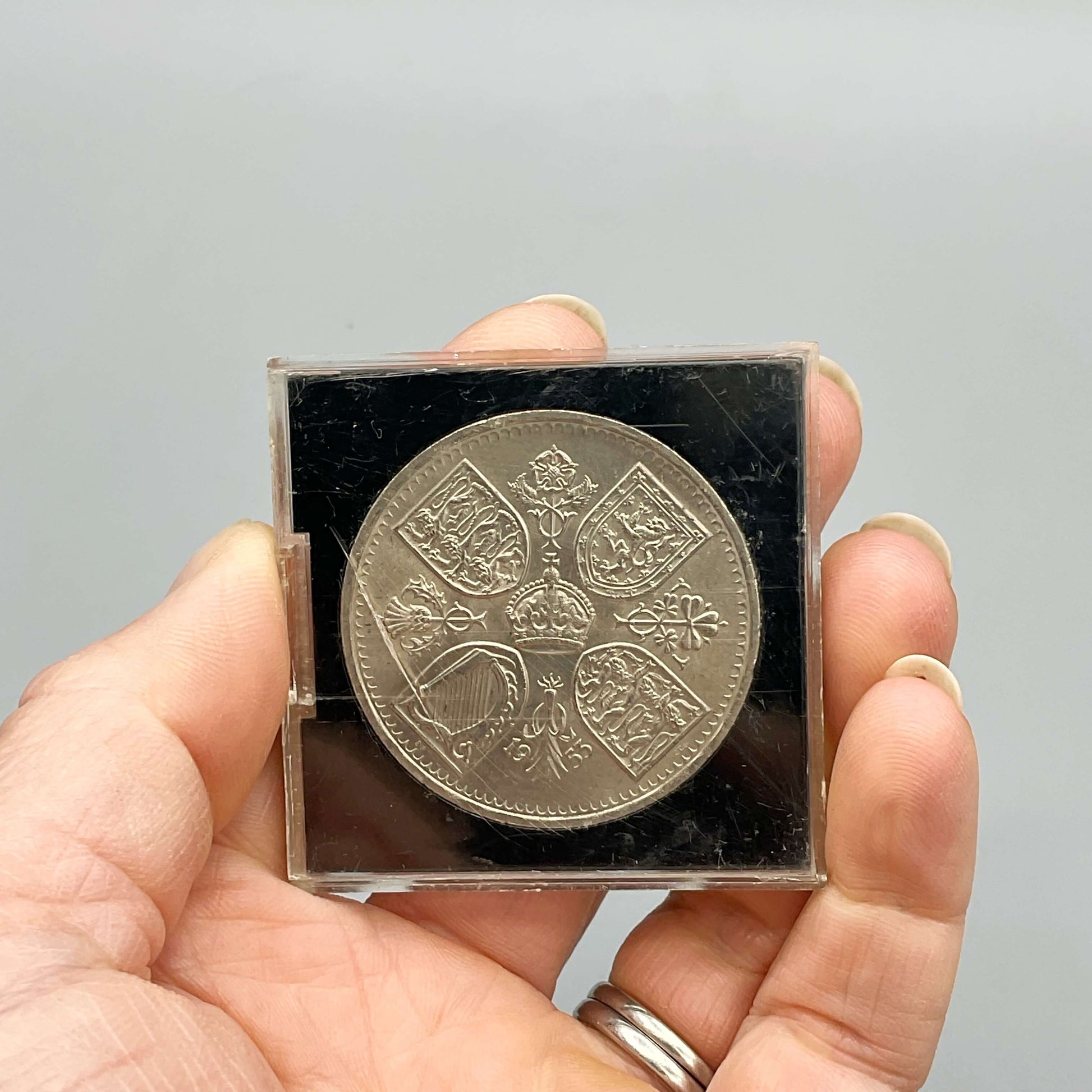 Reverse side of Queen Elizabeth II Coronation Five Shilling Coin in a Perspex Case held in a hand