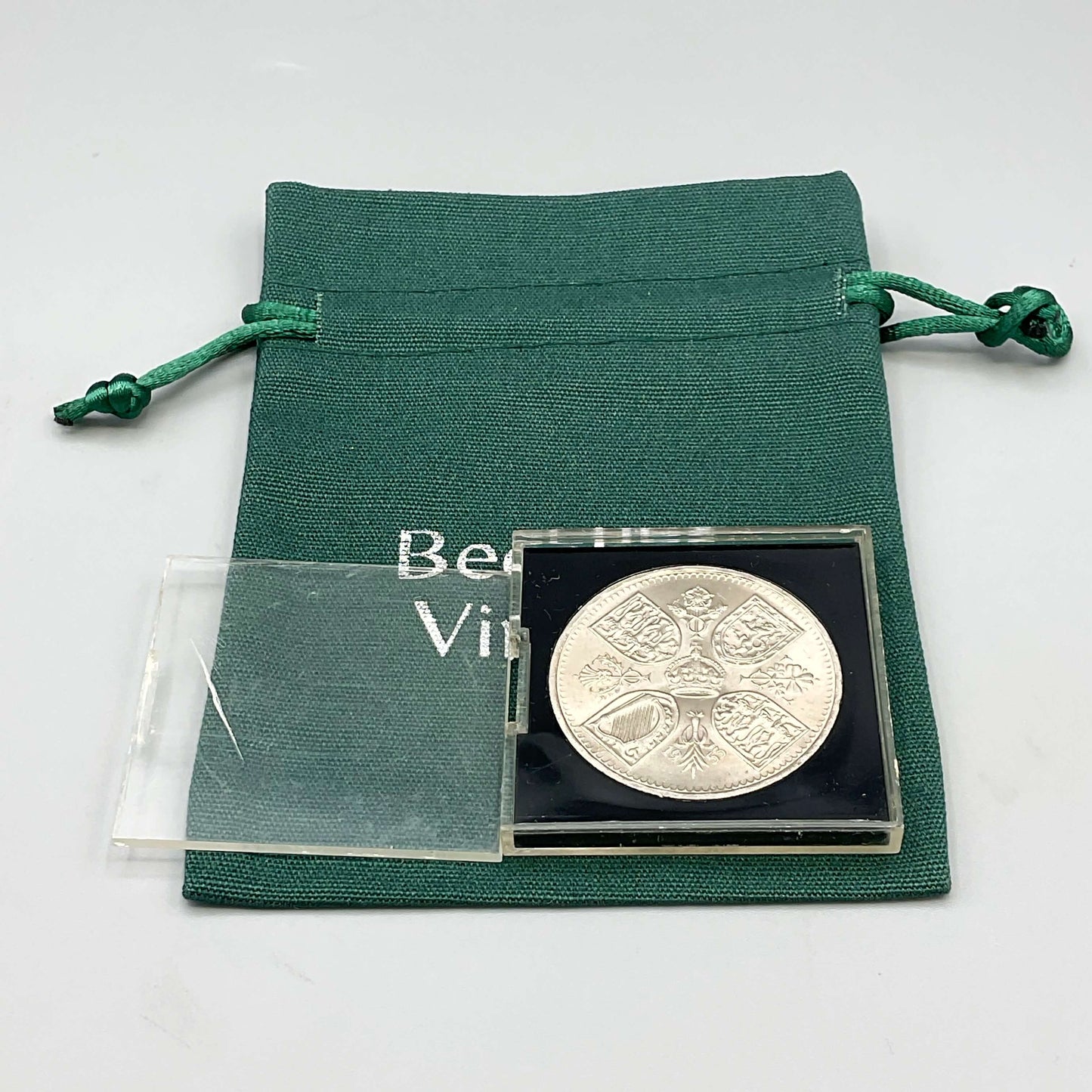 Reverse side of Queen Elizabeth II Coronation Five Shilling Coin in a Perspex Case on a green gift bag With the lid removed 