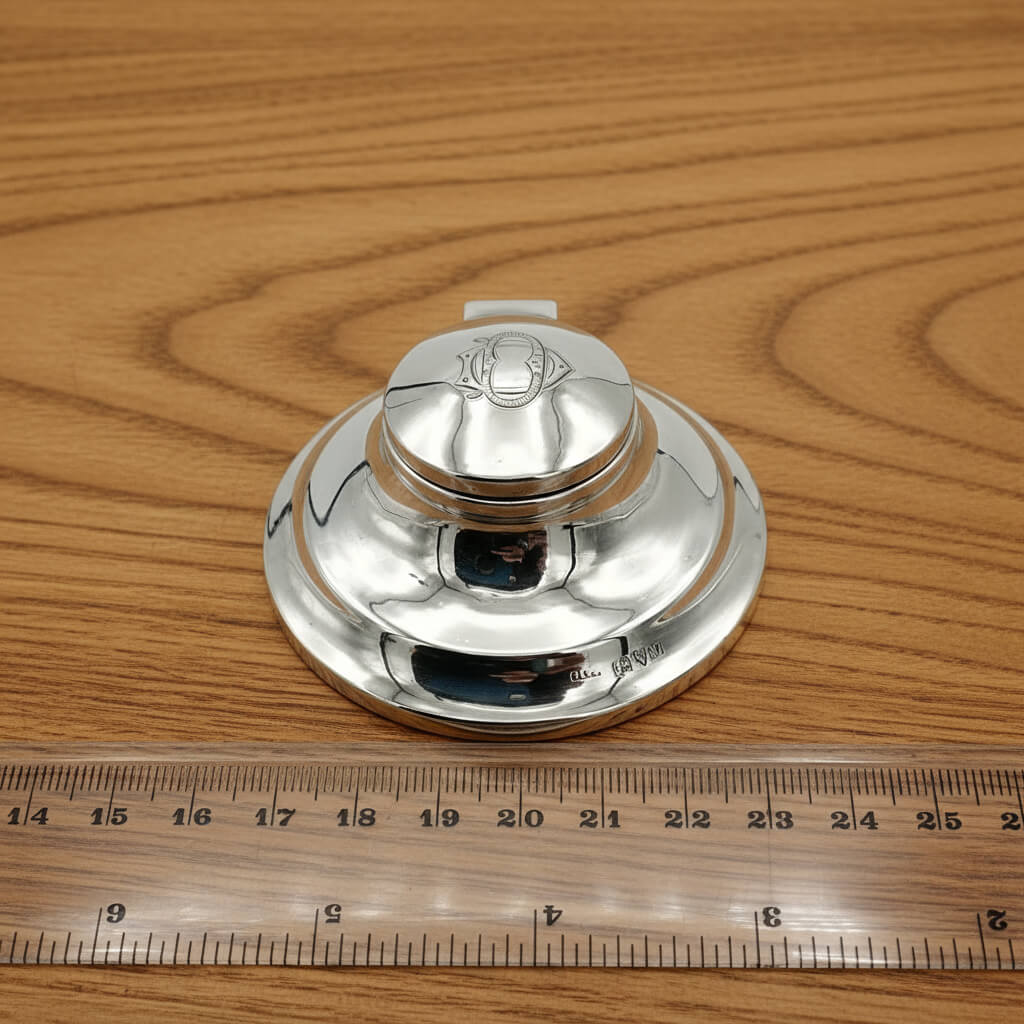 small silver inkwell on a wood table next to a ruler for scale