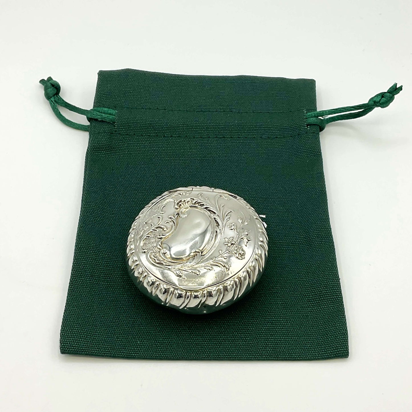 Embossed silver pill box on a green bag