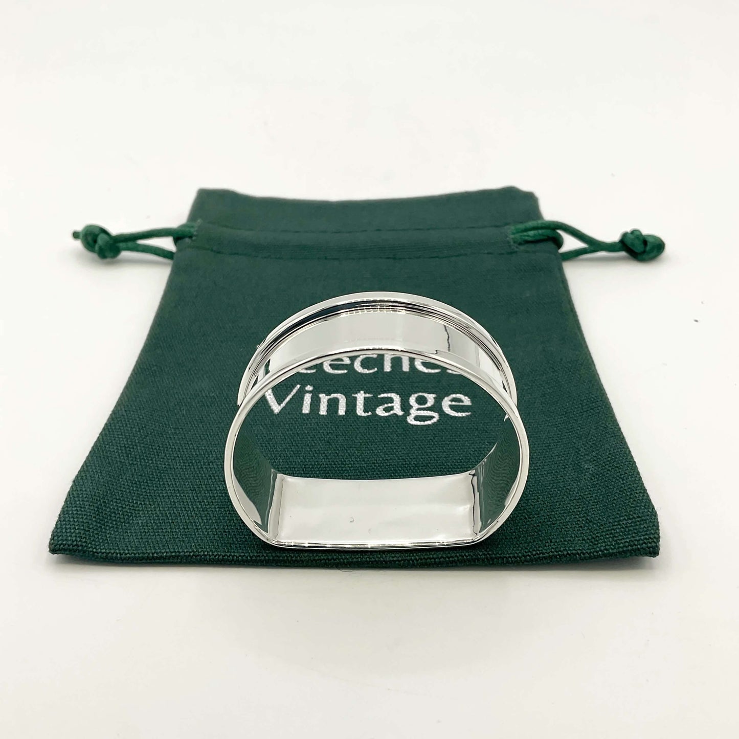 Side view of arch shaped silver napkin ring on a green gift bag on a white background