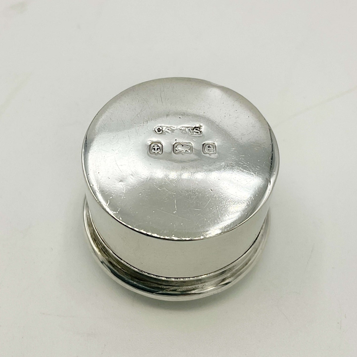 Base of Antique silver pill box showing hallmarks and maker’s mark on a white background