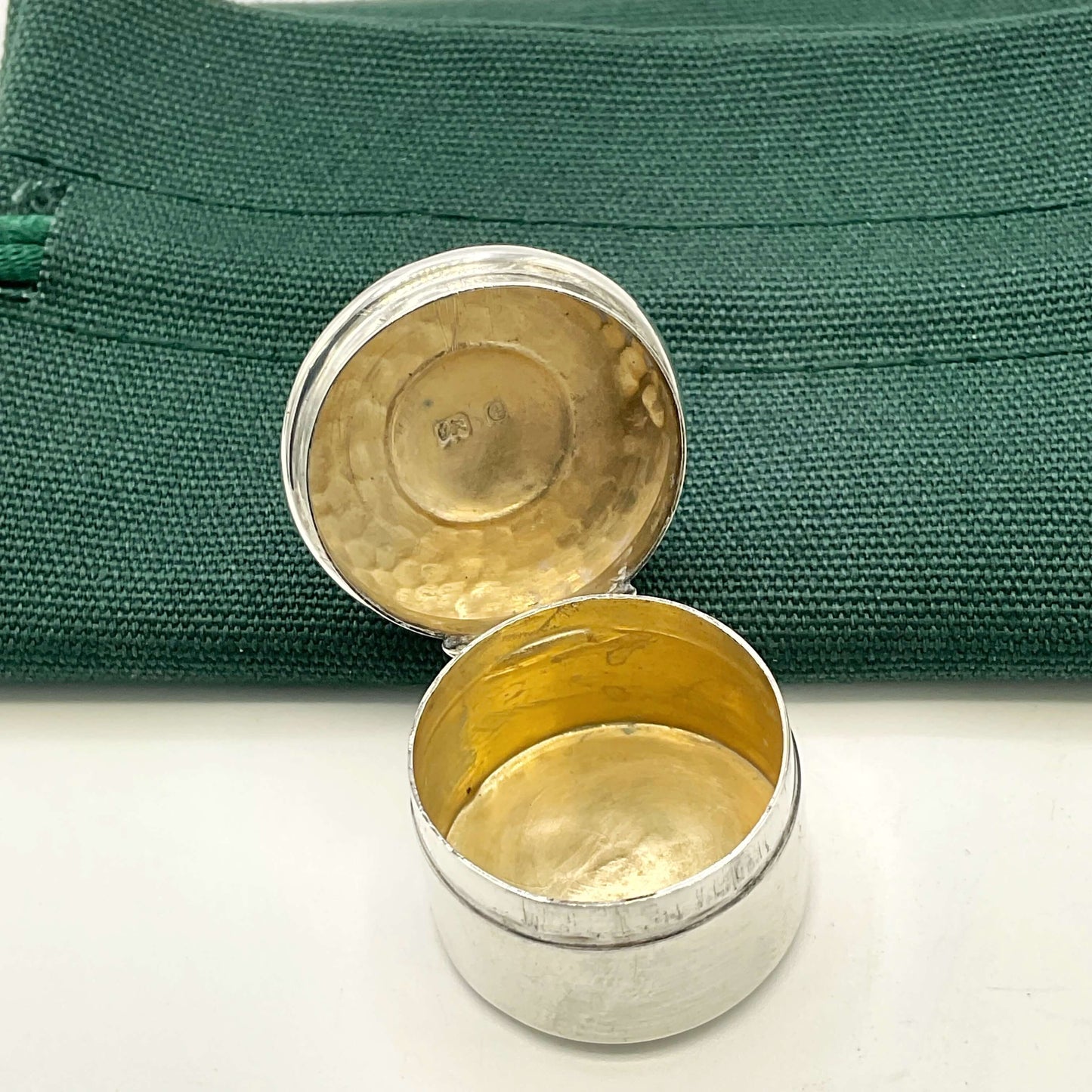 Antique silver pill box with the lid open showing a gold interior next to a green gift bag