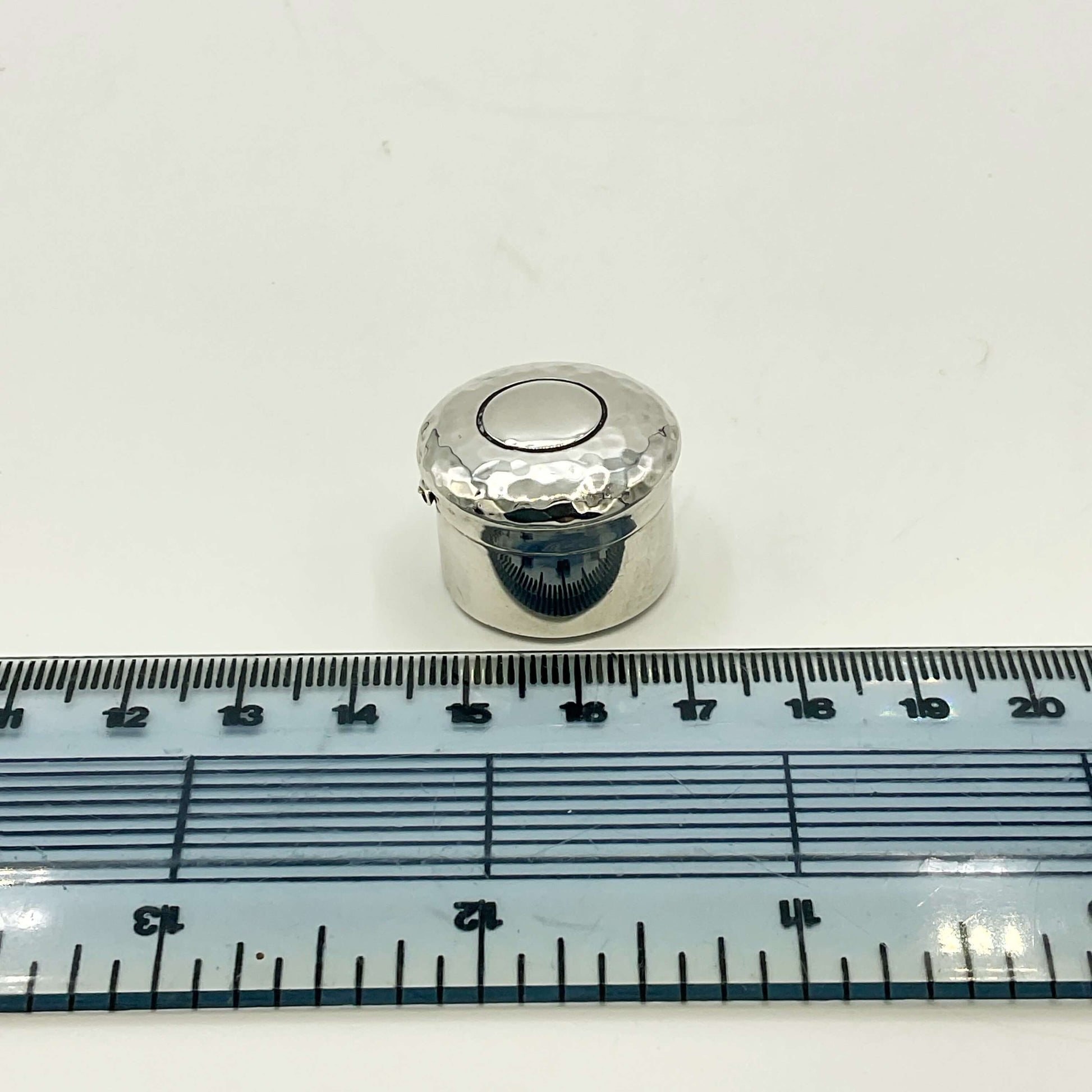 Antique silver pill box on white background next to a ruler showing the size as nearly 2.5cm