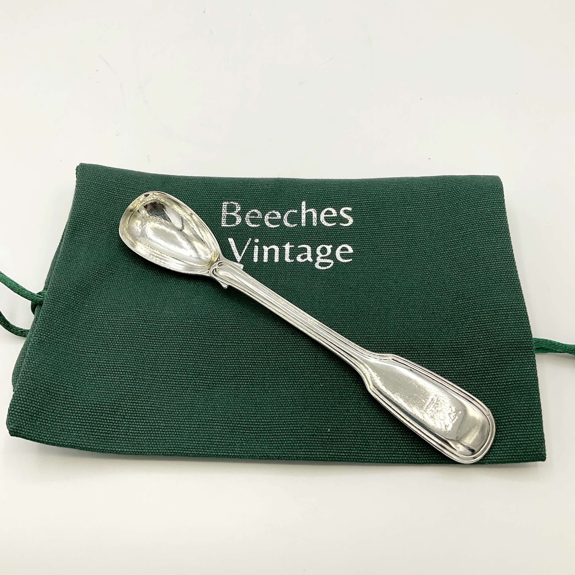 Antique silver mustard spoon on a green gift bag on a white background 