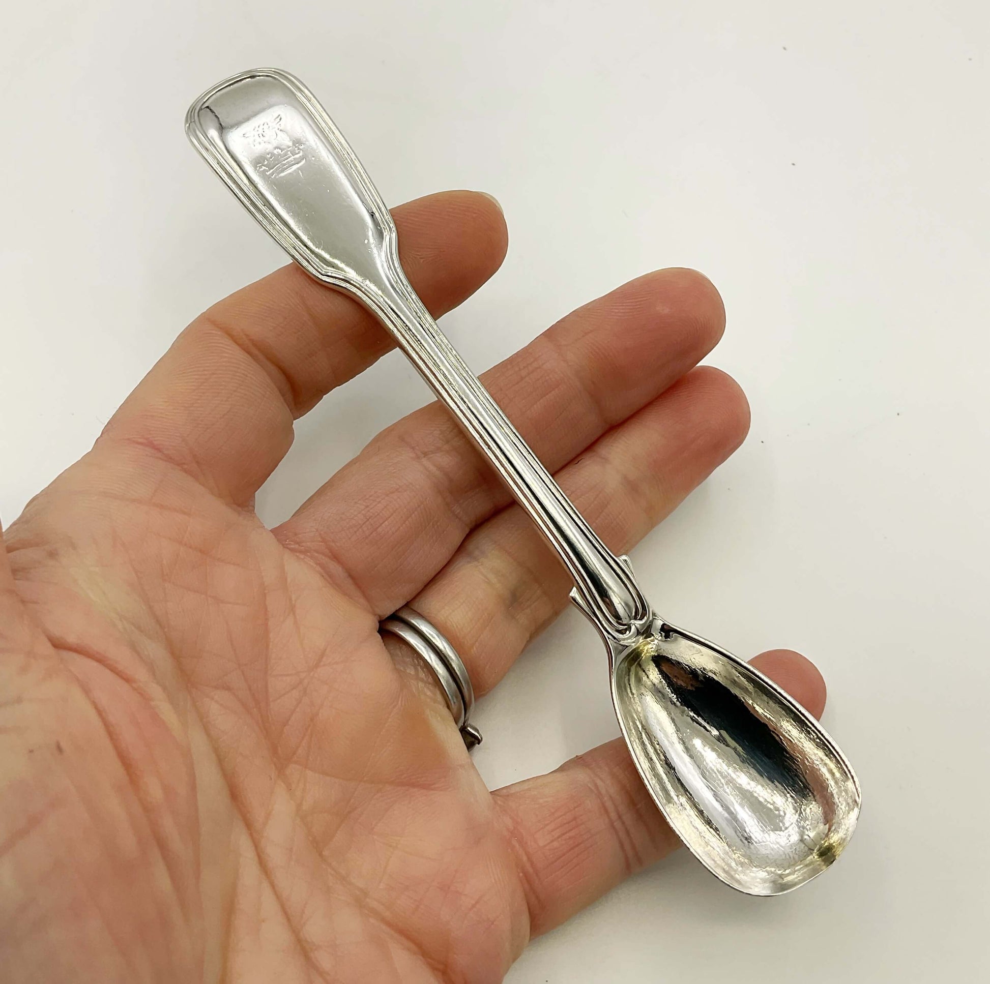 Antique silver mustard spoon held in a hand on a white background 
