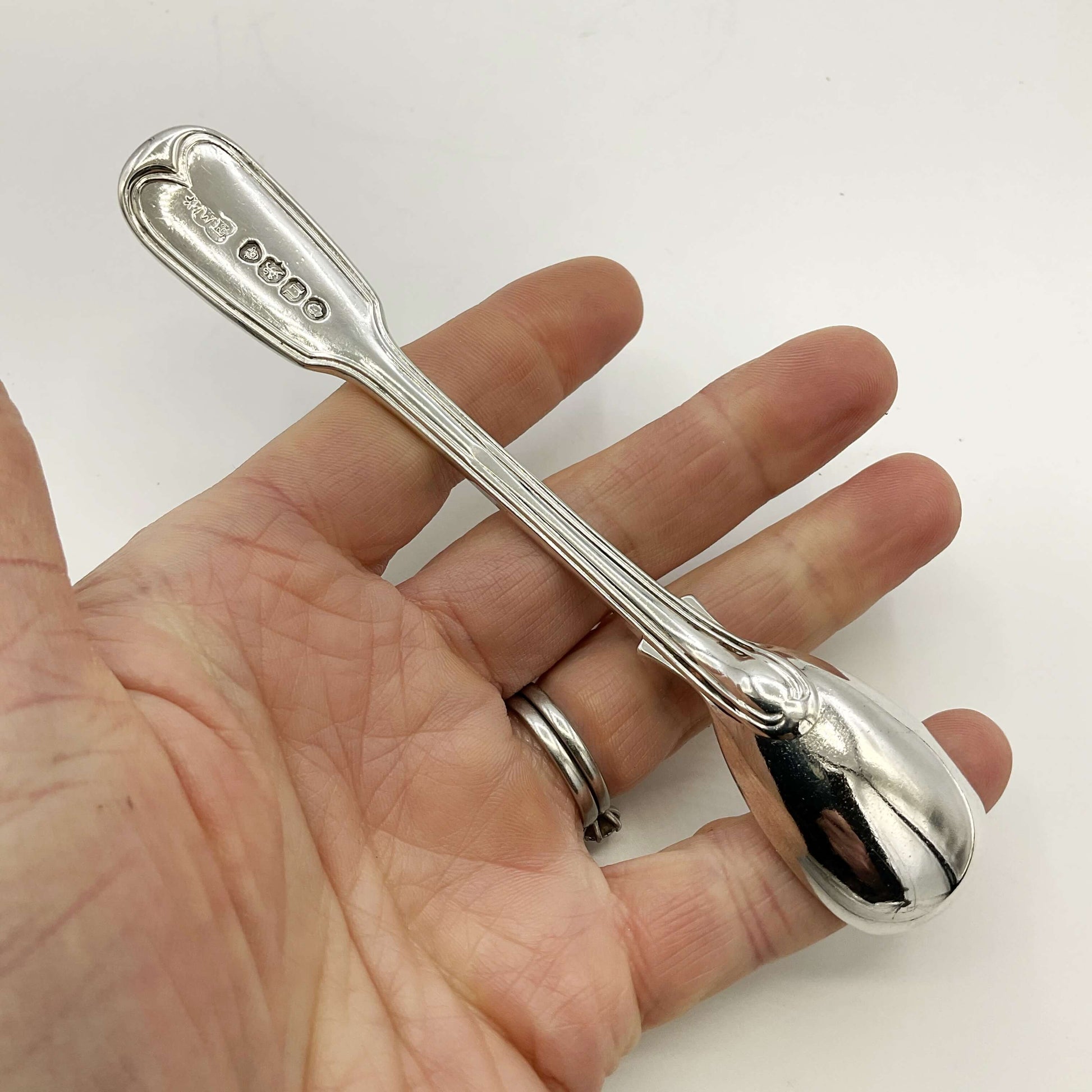 Back of Antique silver mustard spoon held in a hand on a white background 