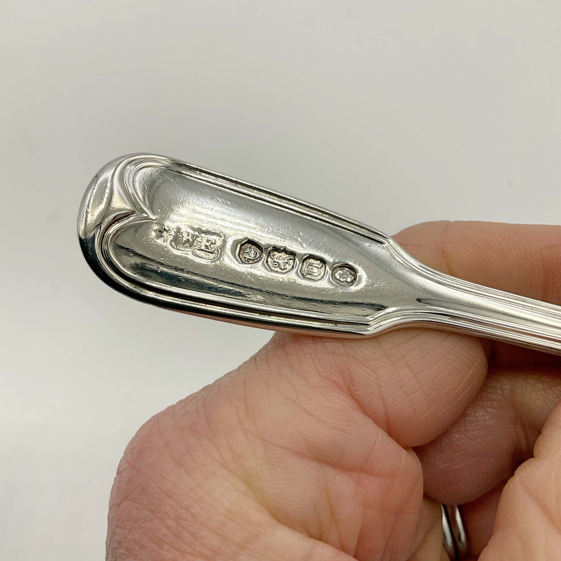 Antique silver mustard spoon held in a hand on a white background showing the hallmarks