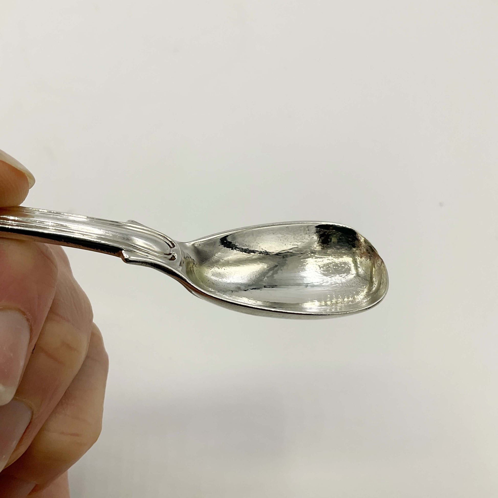 Antique silver mustard spoon held in a hand on a white background 