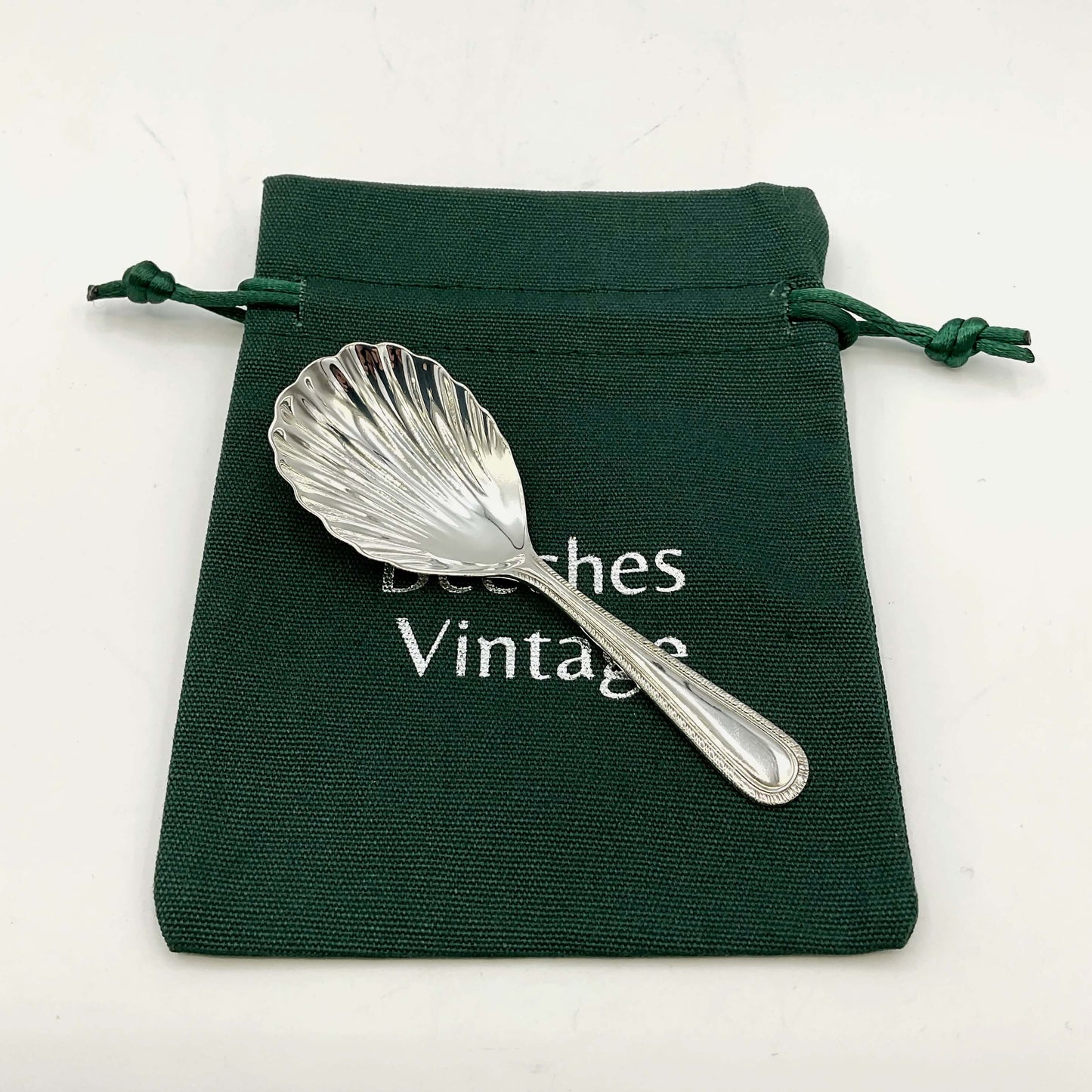 Sterling Silver Scallop Shaped Tea Caddy Spoon on a green gift bag on a white background 