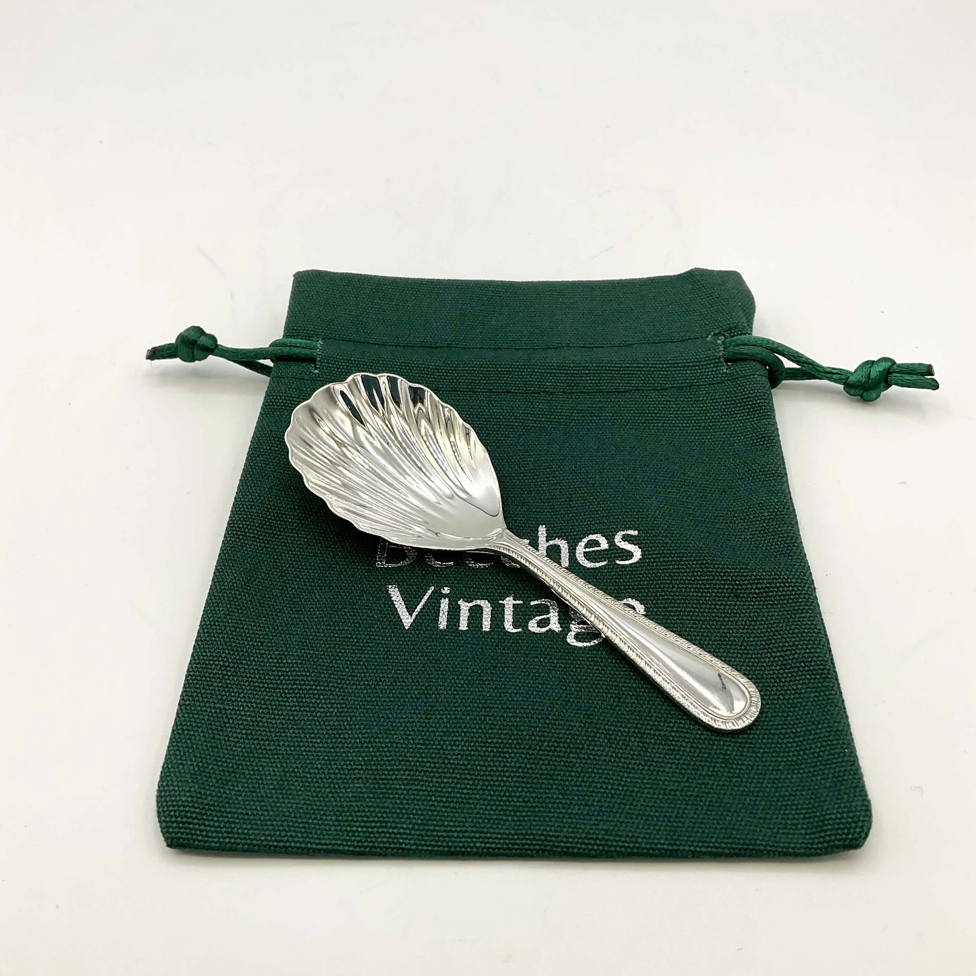 Sterling Silver Scallop Shaped Tea Caddy Spoon on a green gift bag on a white background 