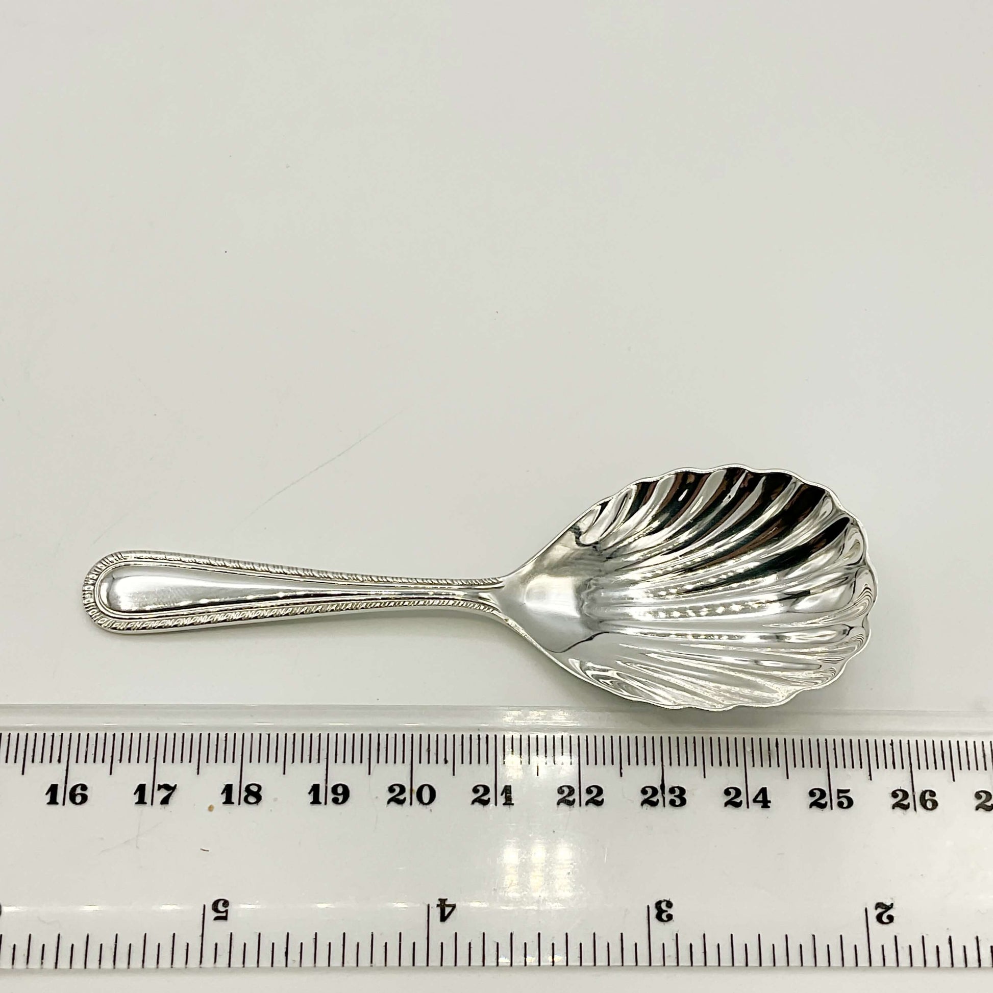 Sterling Silver Scallop Shaped Tea Caddy Spoon on a white background next to a ruler showing the length as 9.5cm