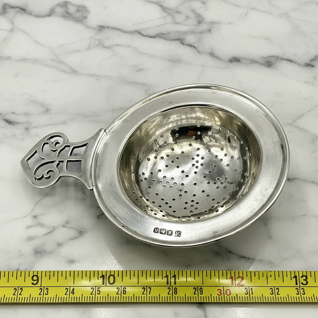 Antique 1925 sterling silver tea strainer with ornate design, from Beeches Vintage, showcasing intricate craftsmanship.