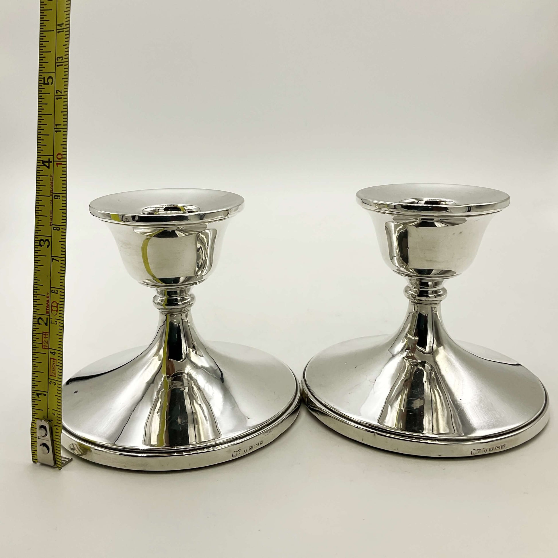 Pair of silver candlestick holders next to a tape measure showing the height as 8.2cm