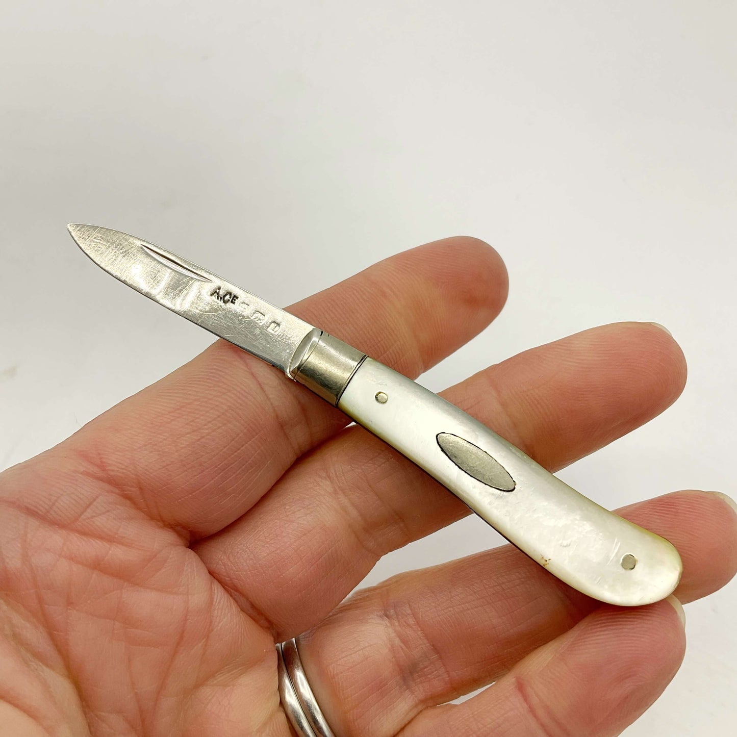 Silver bladed fruit knife with a mother of Pearl handle Held in a hand with a white background