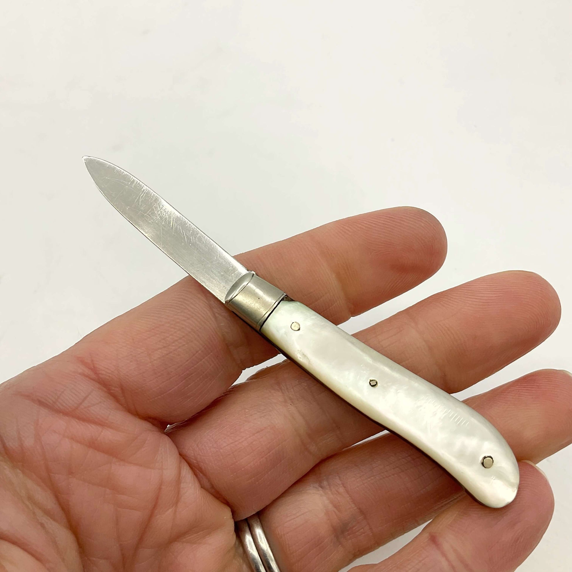 The back of a Silver bladed fruit knife with a mother of Pearl handle held in a hand with a white background 