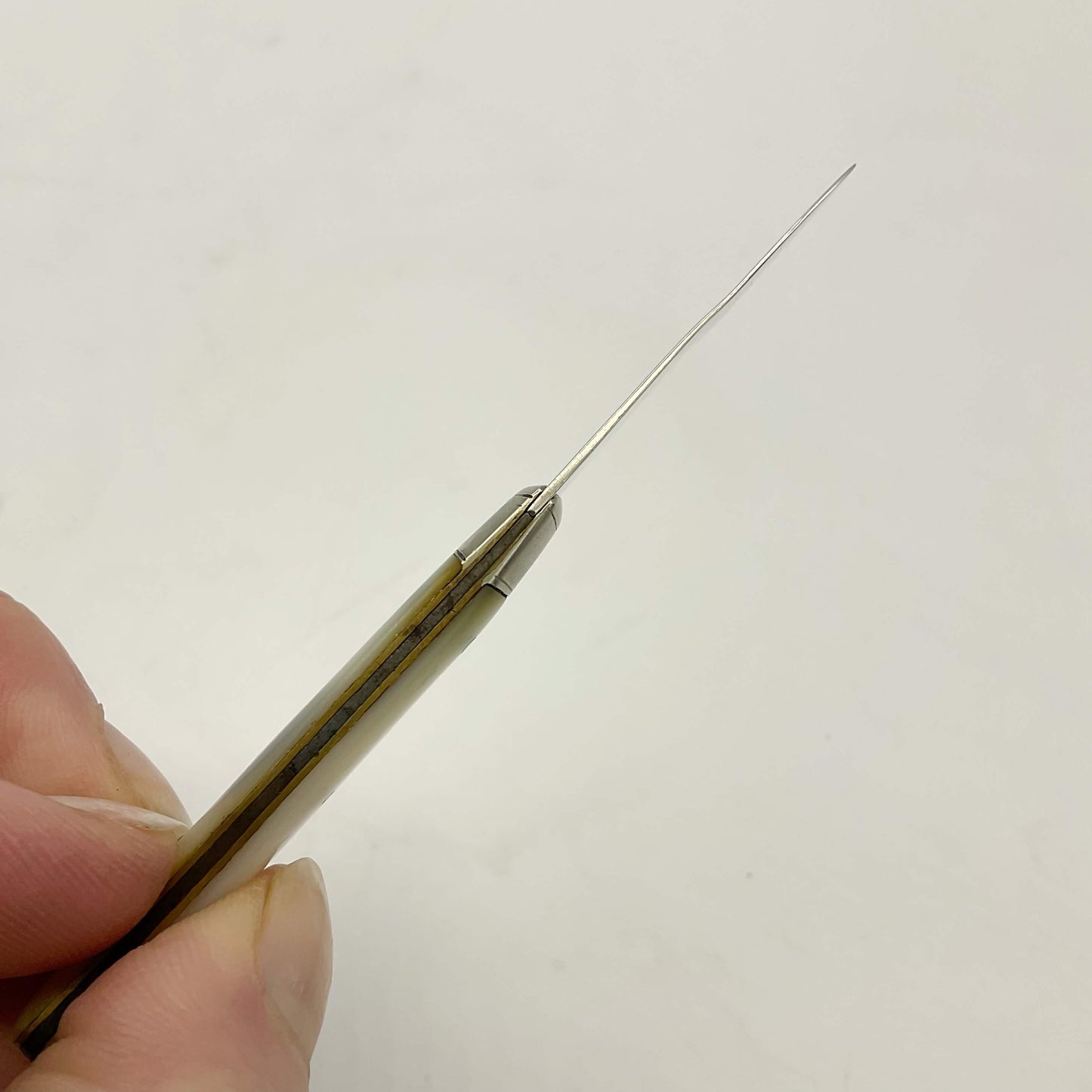 Top view of Silver bladed fruit knife with a mother of Pearl handle showing a small kink to the blade. It’s held in a hand with a white background.
